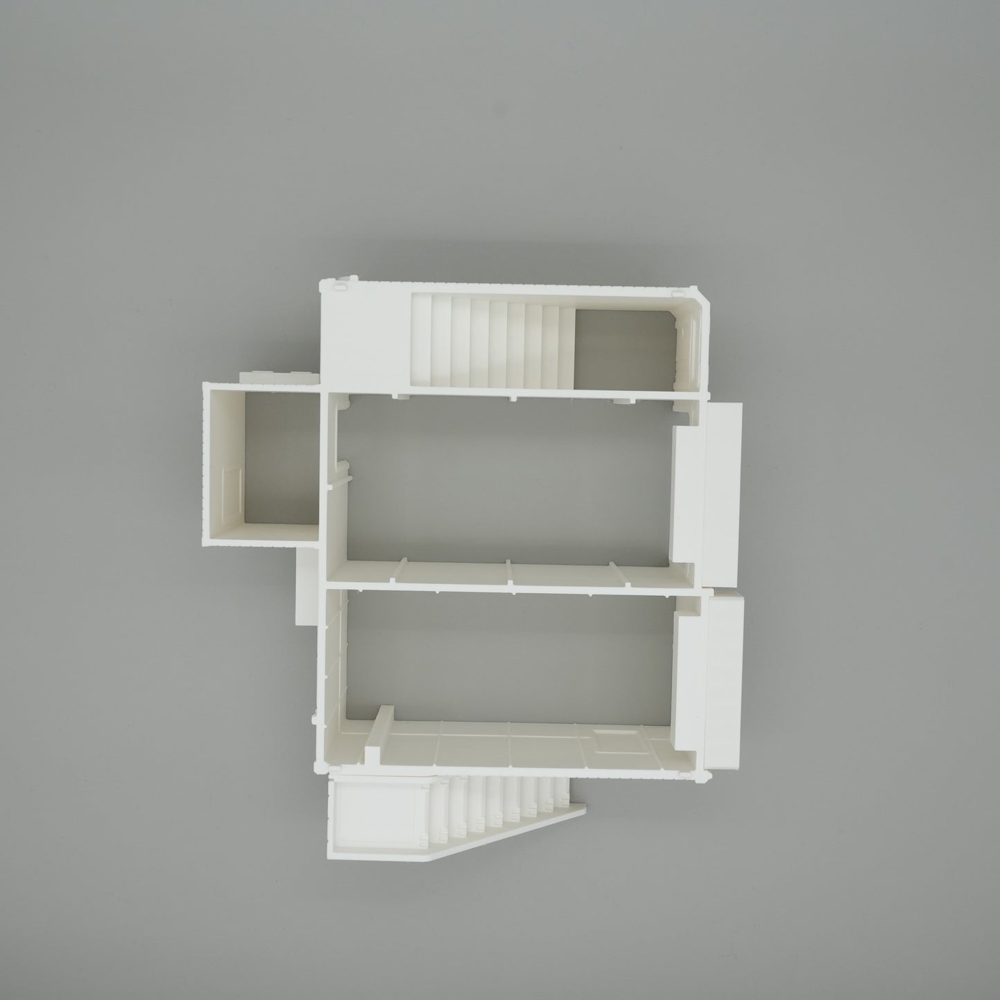 Weißes Modell eines großen Wohnhaus-Grundrisses mit Treppenhaus und mehreren Räumen auf grauem Hintergrund.