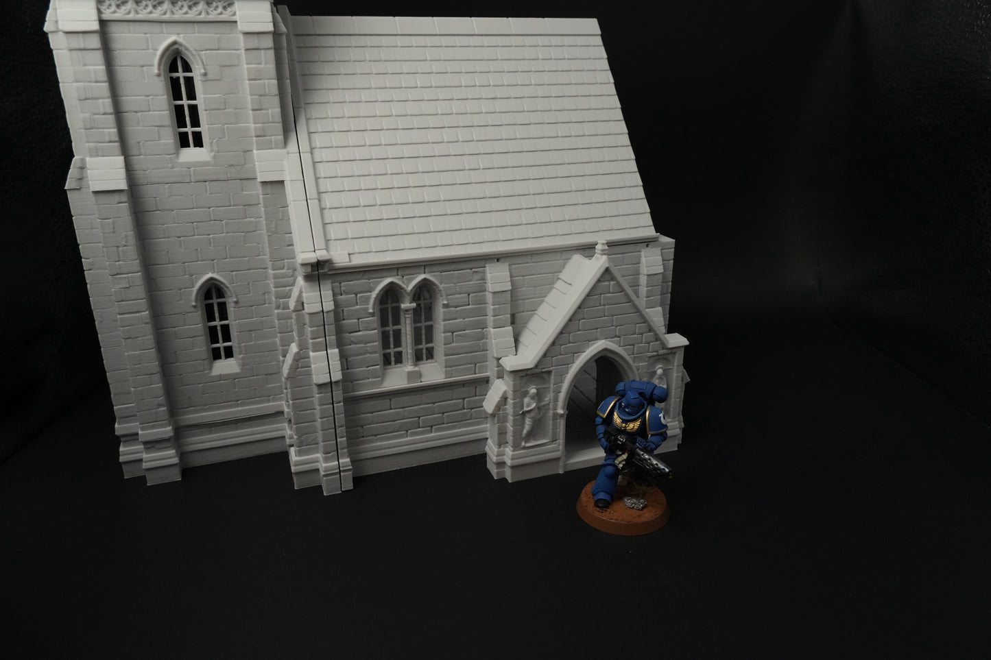 Detailliertes graues mittelalterliches Kirchenmodell mit gotischen Fenstern und steinernen Mauern, daneben Miniaturfigur.