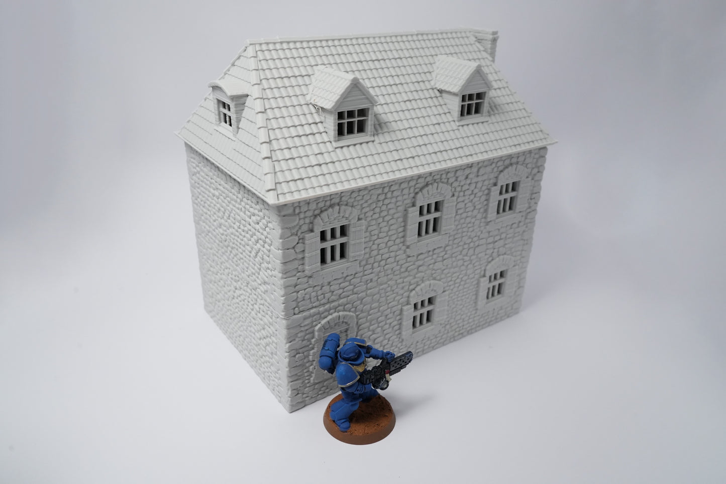 Weißes französisches Farmhaus mit Satteldach und mehreren Fenstern, daneben blaue Spielfigur.