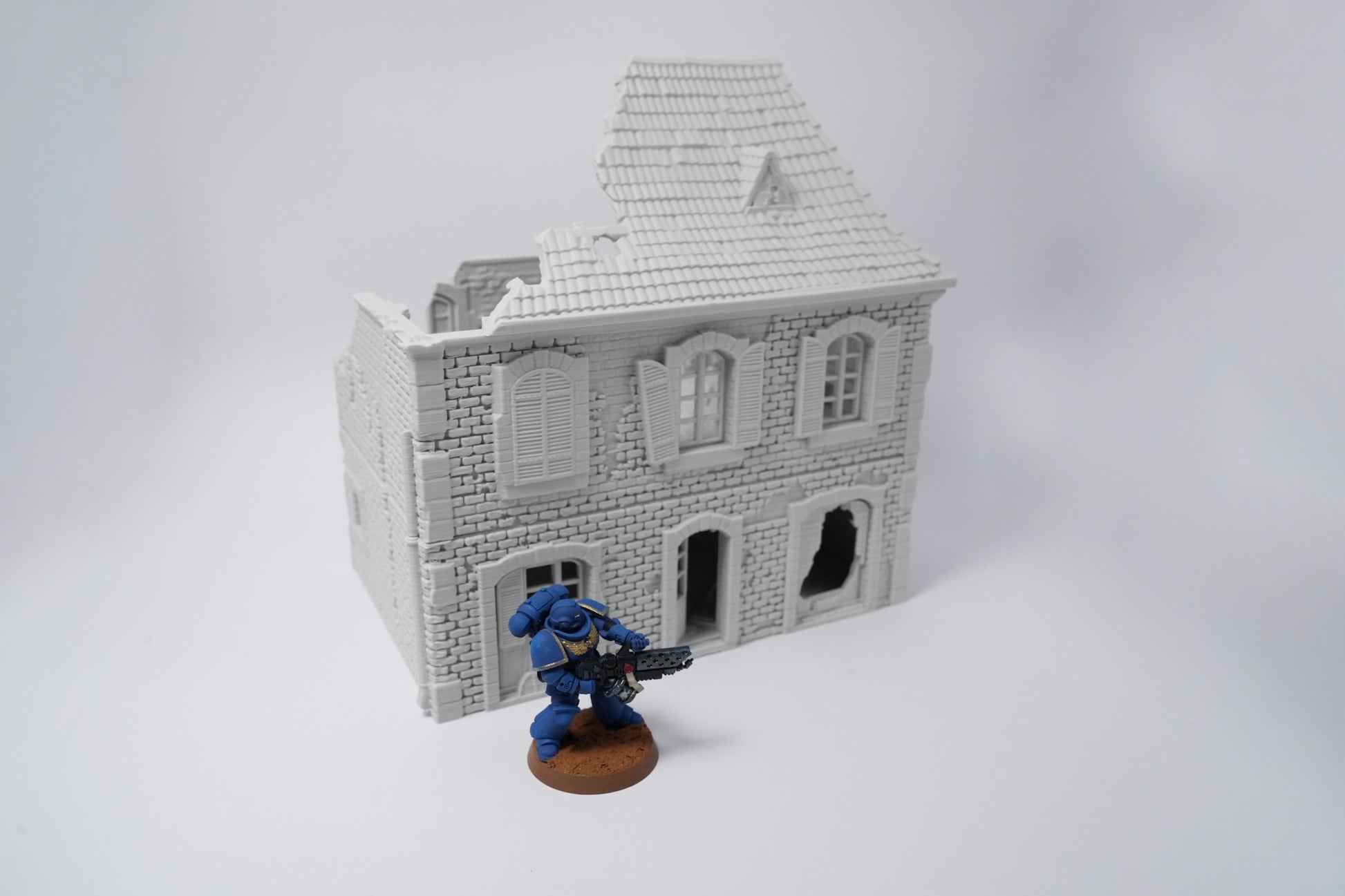 Weißes zweistöckiges Haus in Ruinen mit zerbrochenen Fenstern und beschädigtem Dach, Miniaturmaßstab.