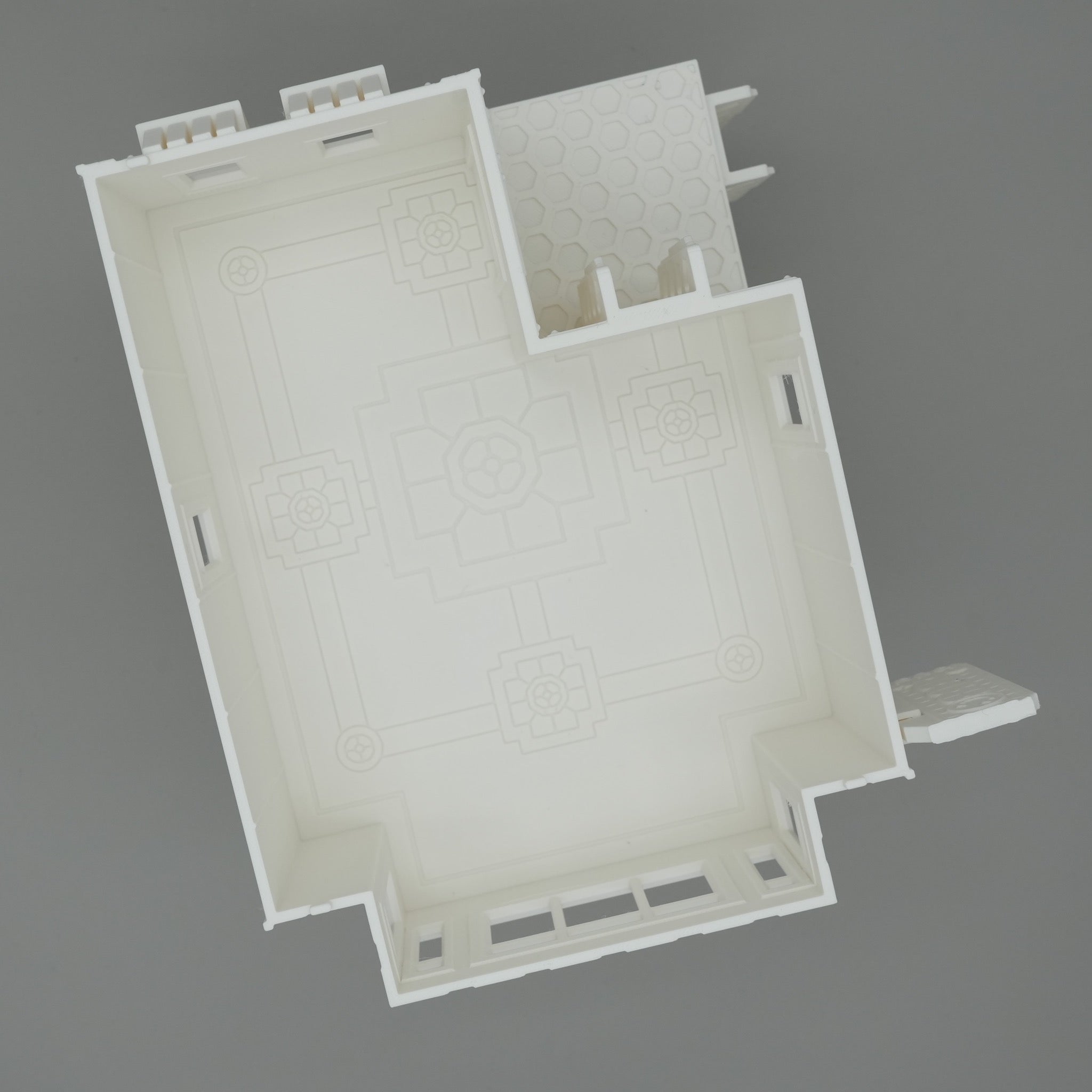 Weißes Modellgebäude mit rechteckigem Grundriss und kleinem Anbau, Fensteröffnungen entlang der Wände.