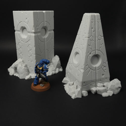 Zwei graue Alien-Obelisken mit futuristischen Gravuren und Felsstücken, daneben bemalter 28mm Space Marine-Figuren-Maßstab.
