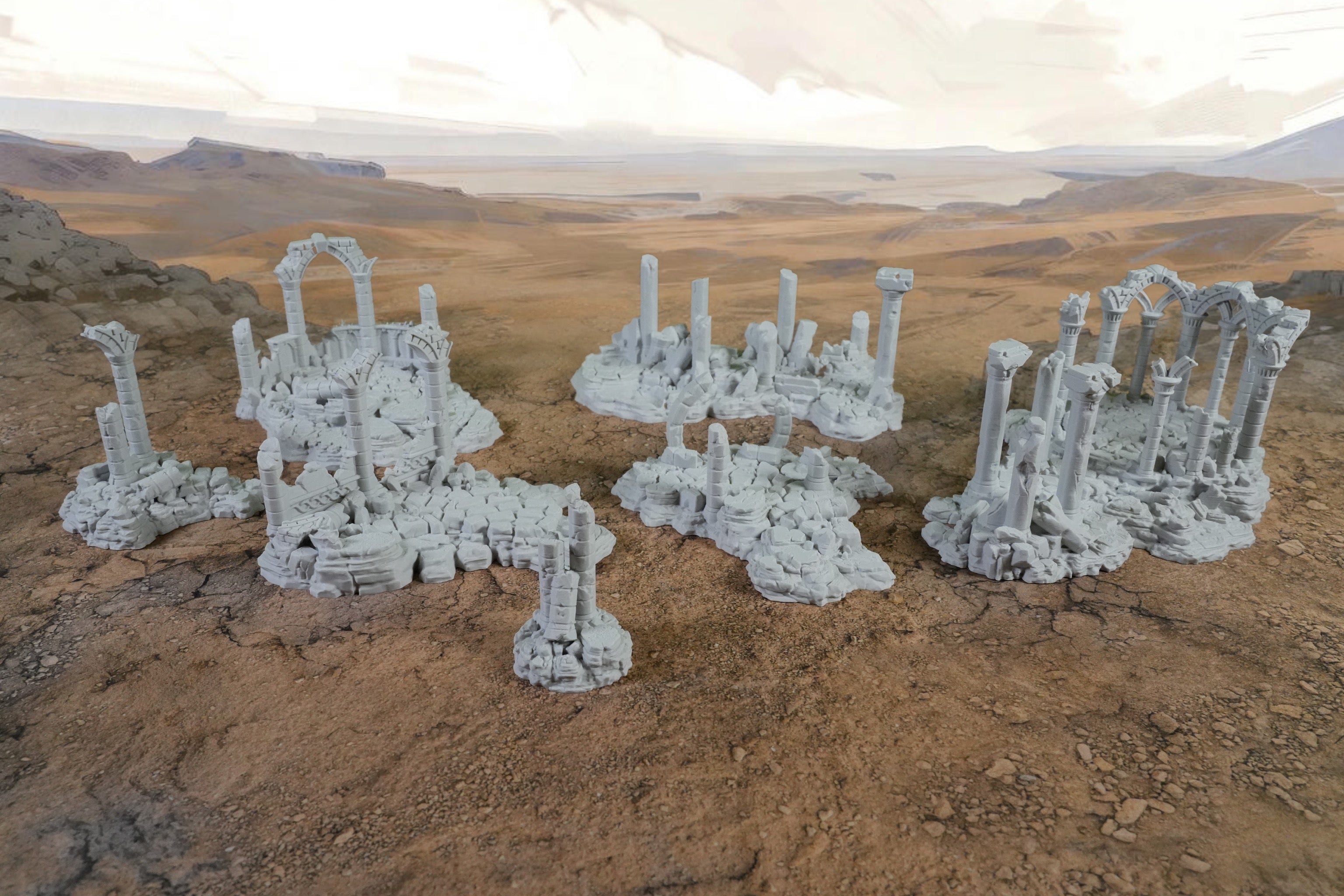 Graue, verwitterte Miniaturruinen mit Säulen und zerfallenen Mauern auf wüstenähnlichem Untergrund.