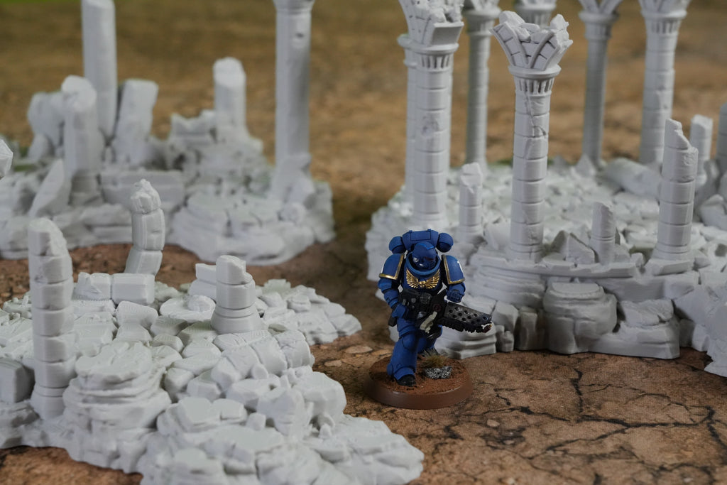 Graue zerfallene Ruinen mit Säulen und Mauern, blauer Miniaturfigur im Vordergrund.