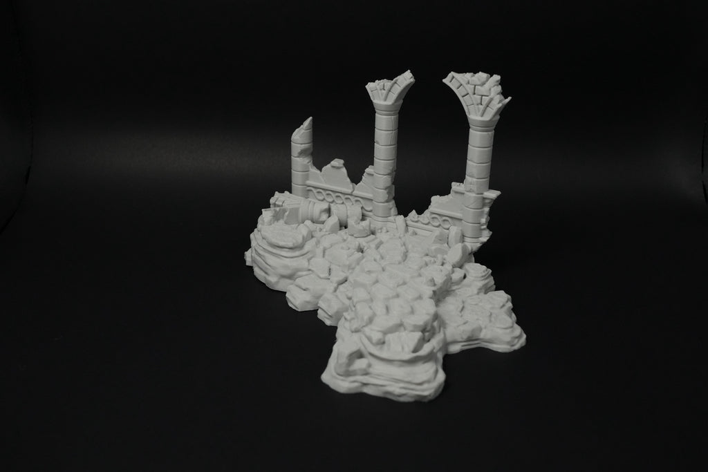 Weißes Modell verwitterter Ruinen mit zerbrochenen Säulen auf unebenem Grund.