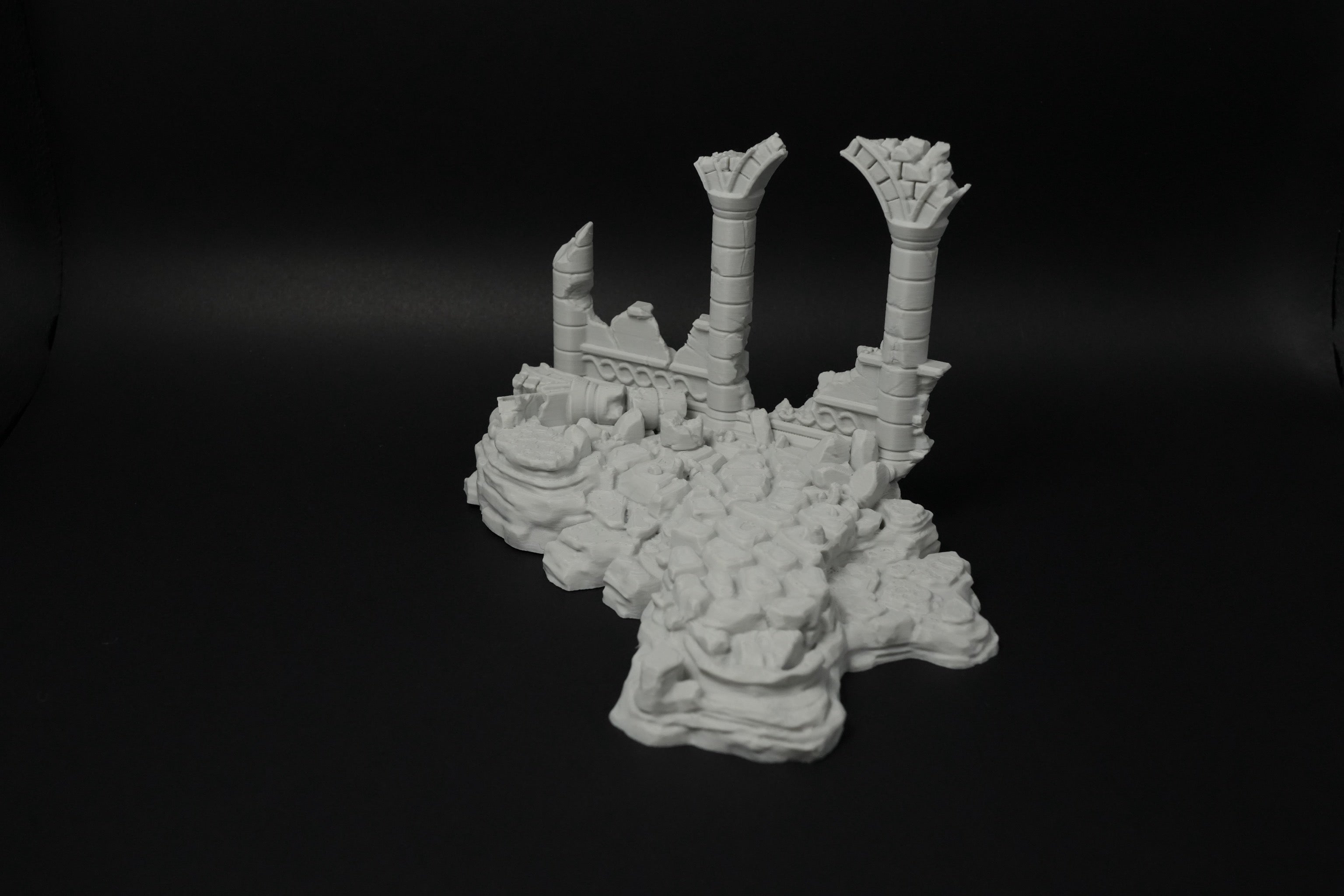 Weißes Modell verwitterter Ruinen mit zerbrochenen Säulen auf unebenem Grund.