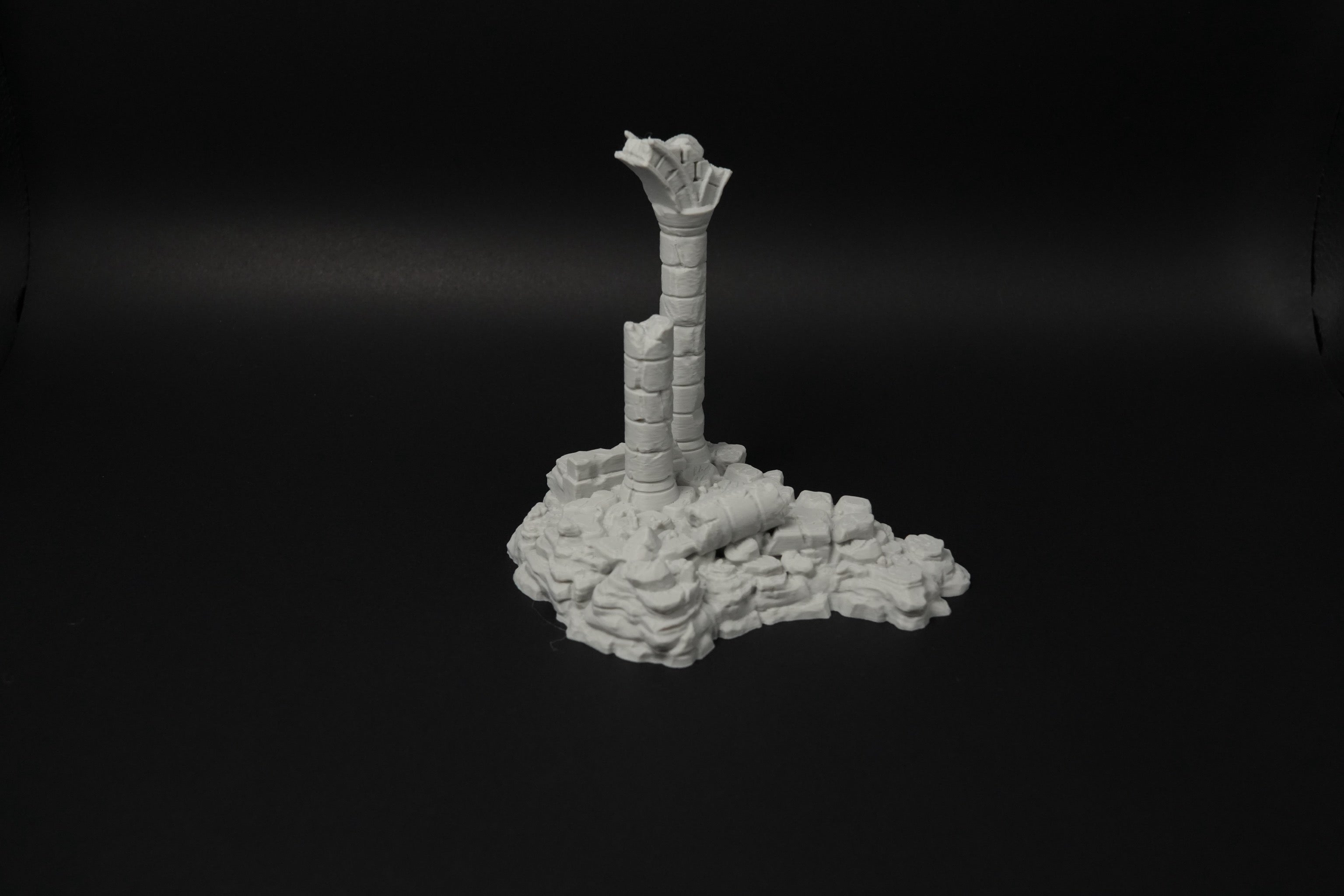 Verwitterte graue Ruinen mit zerbrochener Säule auf unebenem Boden aus Steinen und Trümmern in 28mm Maßstab.