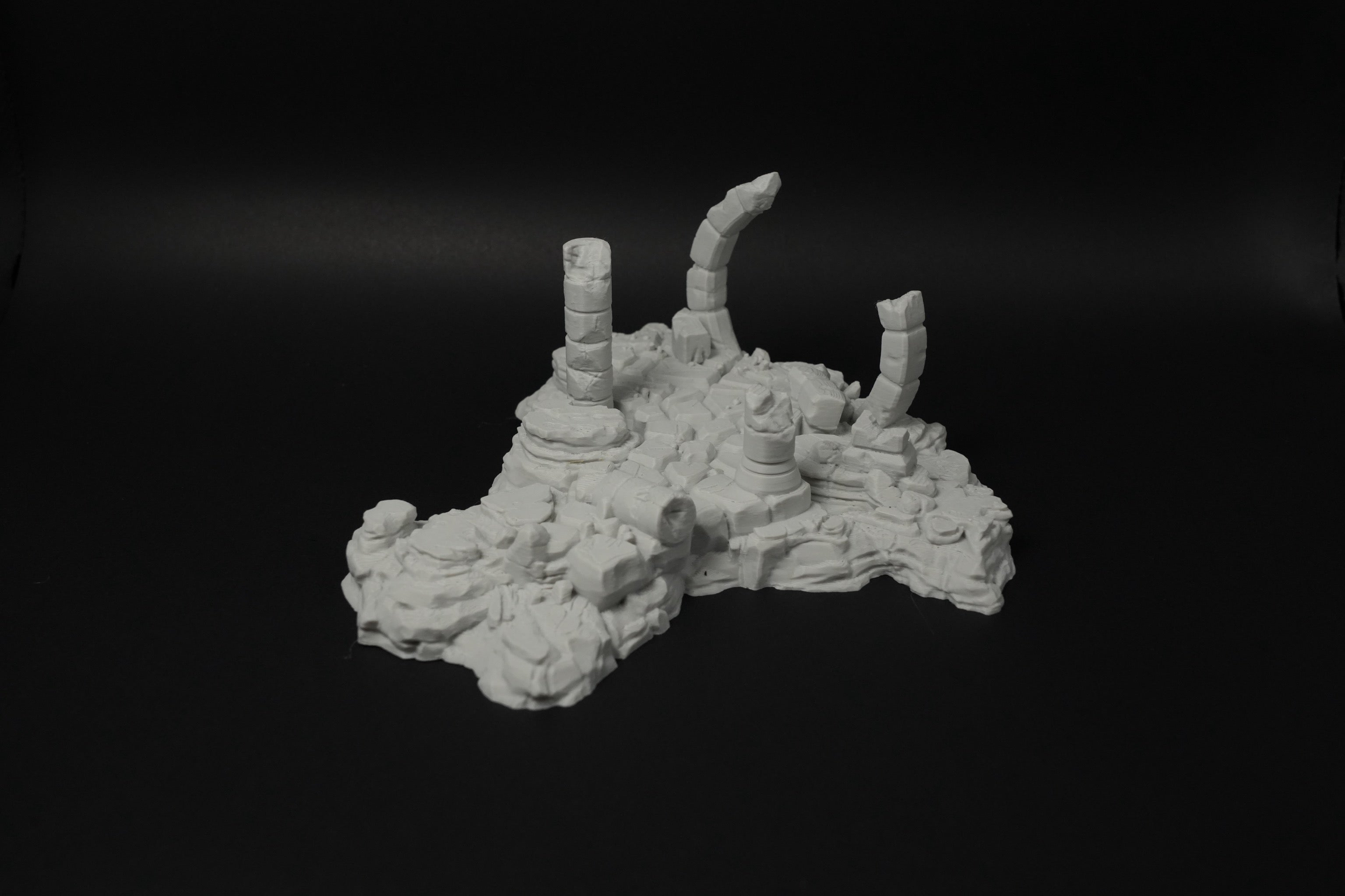 Graue Miniatur-Verwitterte Ruinen mit zerbrochenen Säulen und unebener Struktur auf schwarzem Hintergrund.