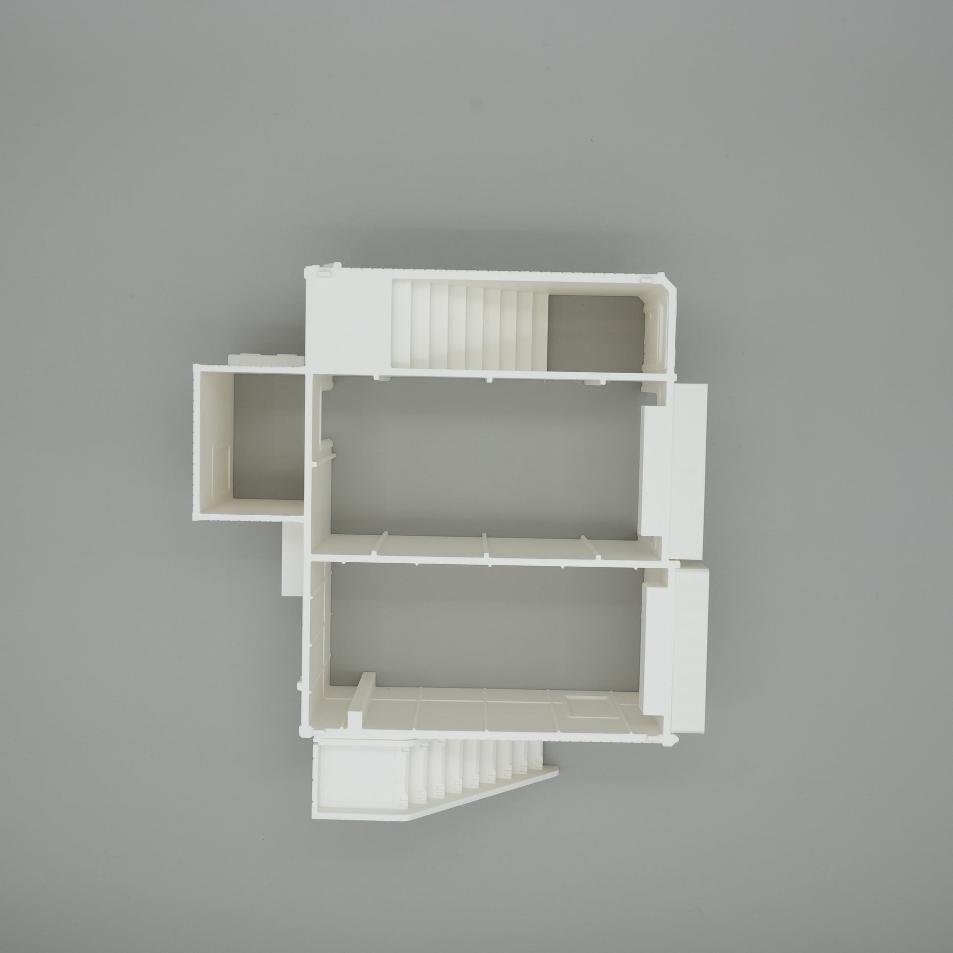 Weißes Modell eines großen Wohnhaus-Grundrisses mit Treppenhaus und mehreren Räumen auf grauem Hintergrund.