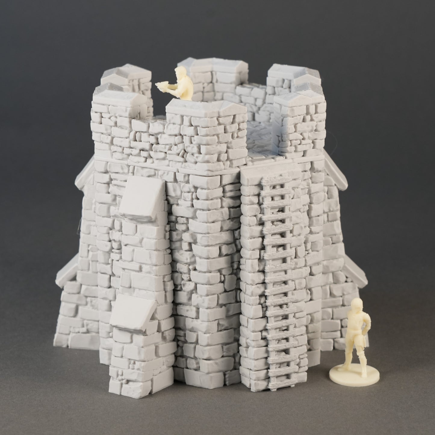 Grauer, detaillierter Spielzeugburg-Turm mit Zinnen und Steinfassaden, daneben Miniaturfigur.
