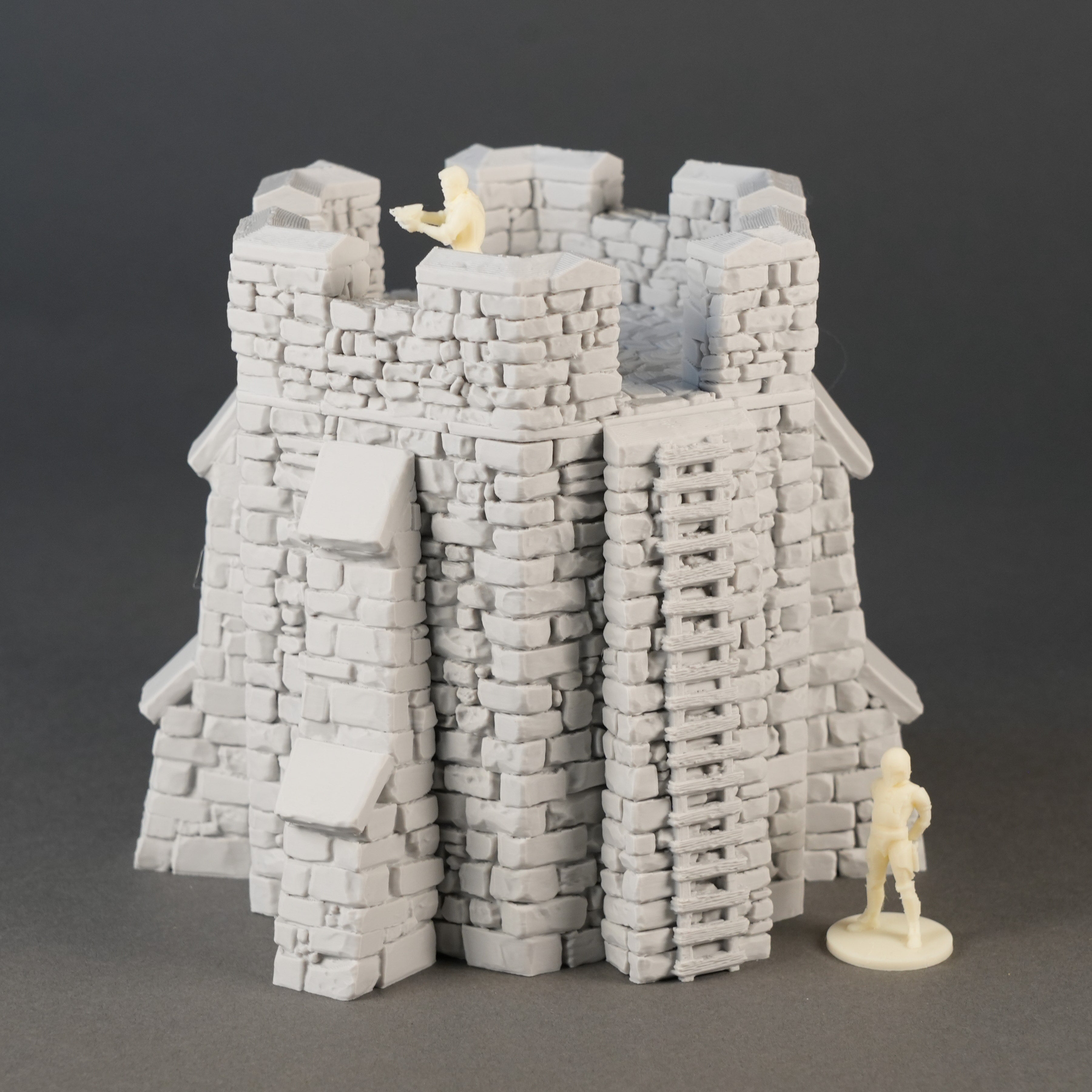 Grauer, detaillierter Spielzeugburg-Turm mit Zinnen und Steinfassaden, daneben Miniaturfigur.