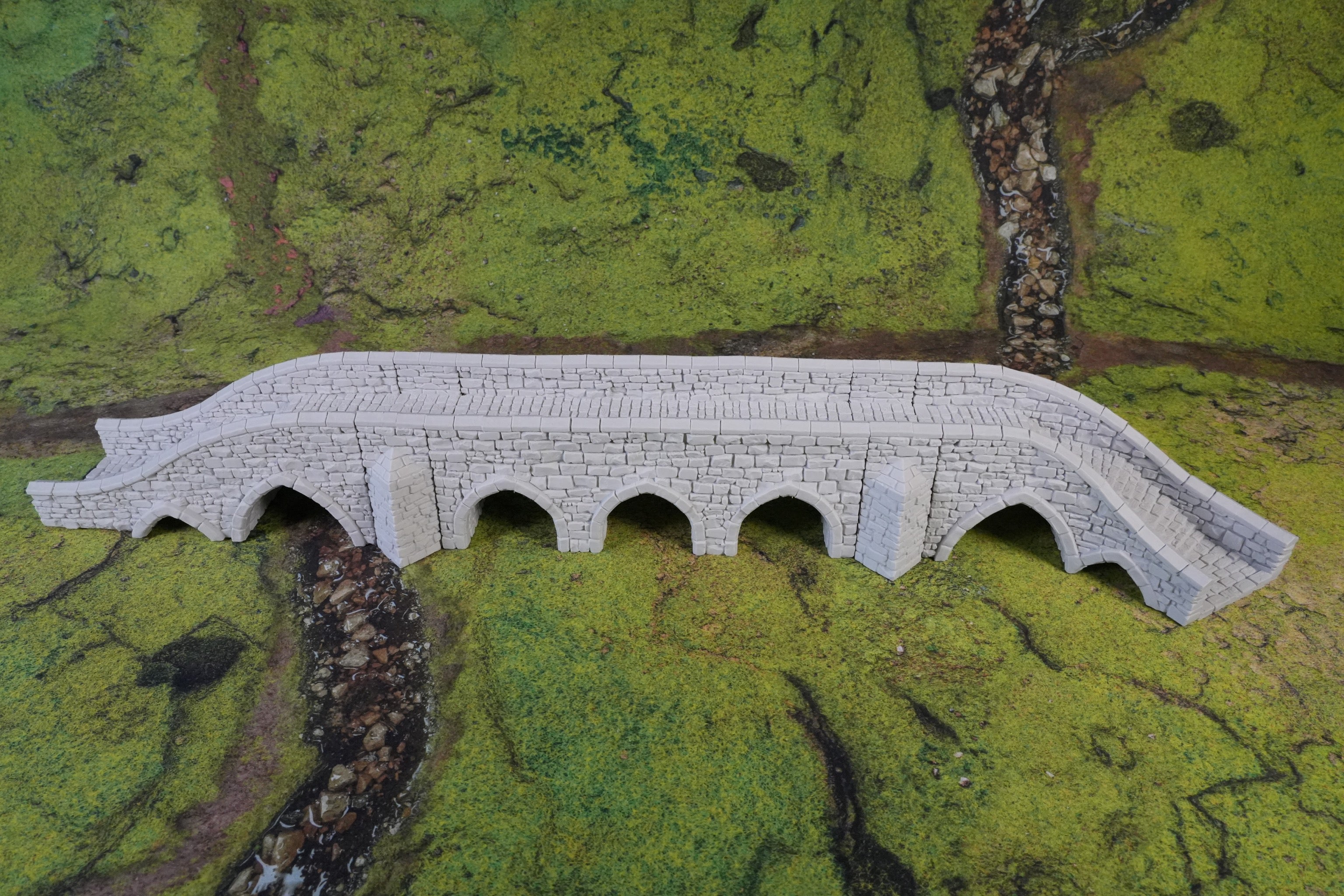 Modellbrücke aus grauem Stein mit fünf Bögen auf grünem Spielfeld.