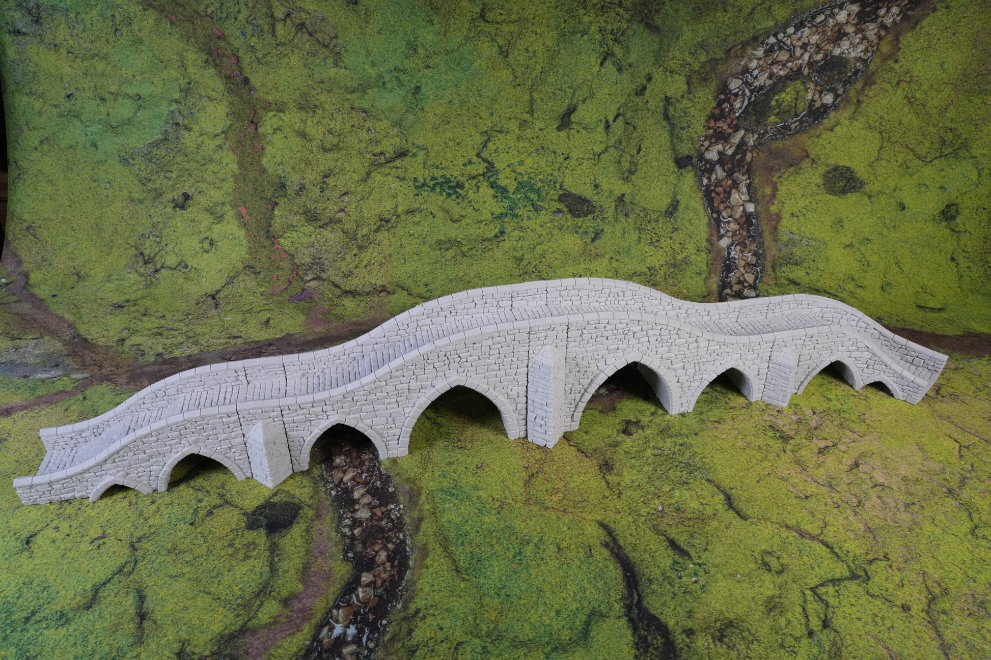 Helle Steinbogenbrücke mit fünf Bögen auf grünem Terrain aus Spielmaterial.