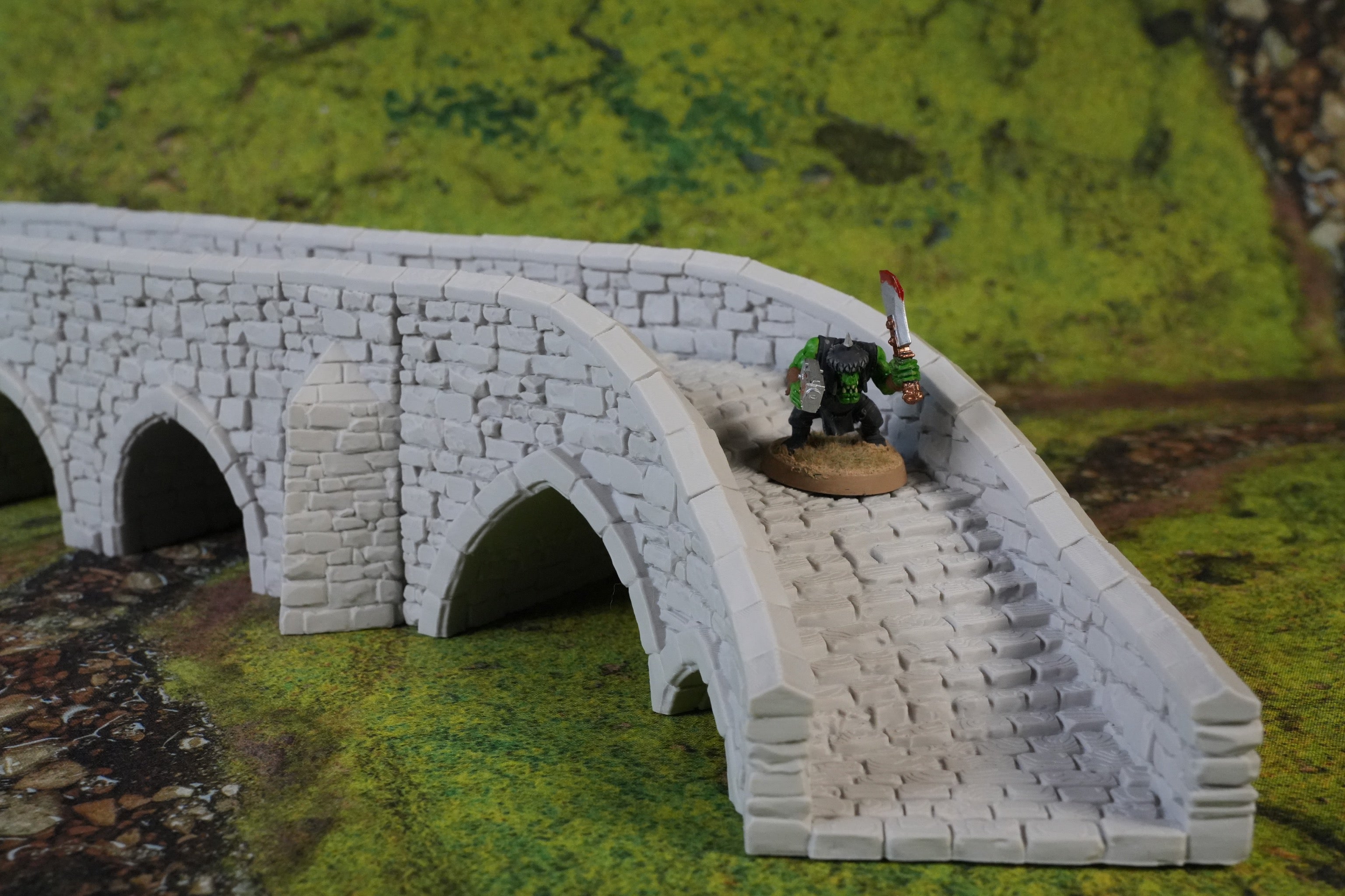 Graue Steinbogenbrücke mit Steinstufen und Miniaturfigur auf grünem Landschaftsuntergrund.