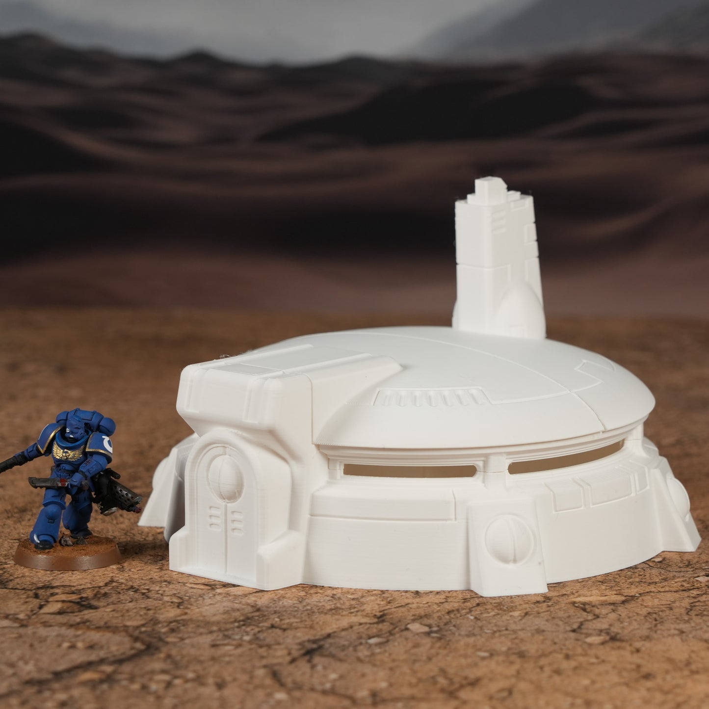 Weißer futuristischer Rundbunker mit Turm und Eingang, daneben blauer Miniatursoldat auf Wüstenboden.