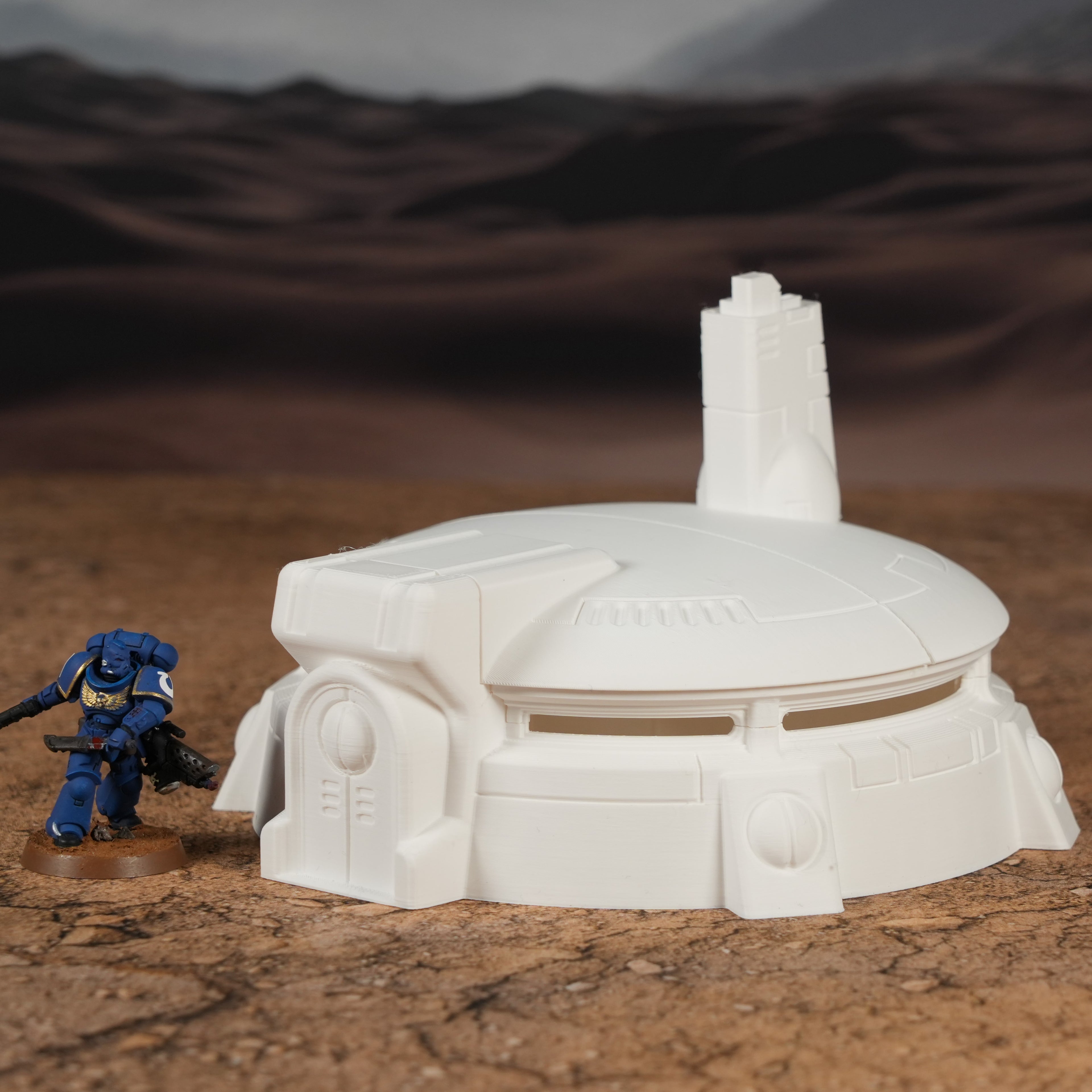 Weißer futuristischer Rundbunker mit Turm und Eingang, daneben blauer Miniatursoldat auf Wüstenboden.