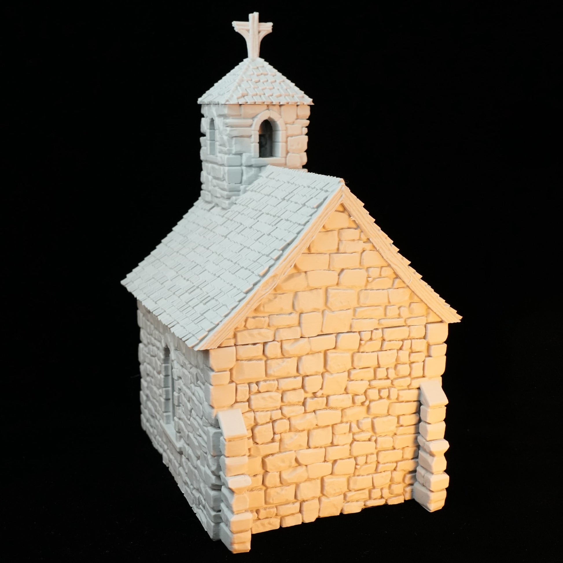 Kleine Steinkapelle mit Kreuz auf spitzem Dach und Fensteröffnung.