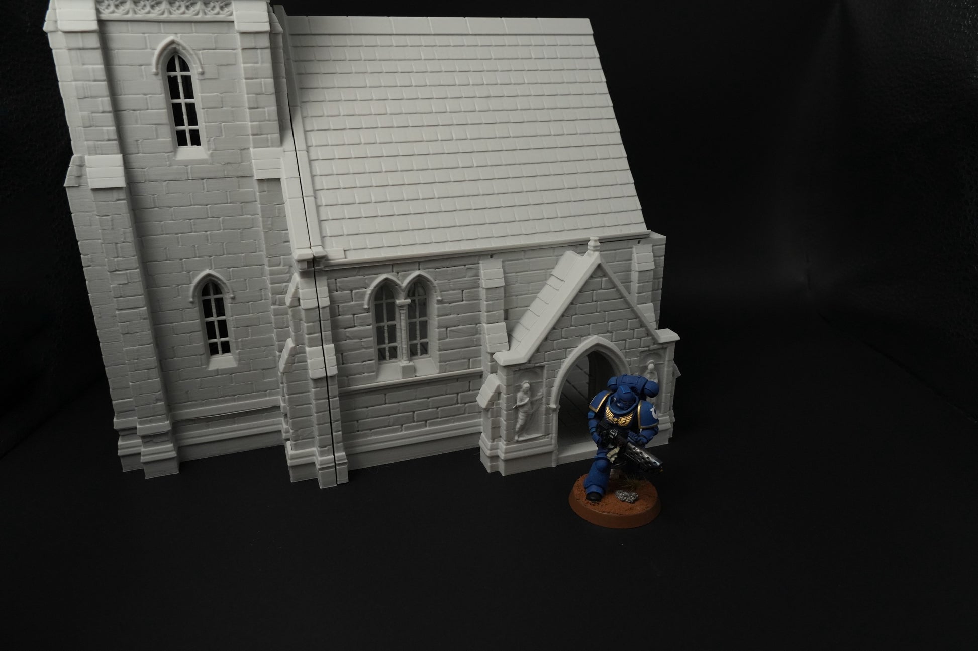 Detailliertes graues mittelalterliches Kirchenmodell mit gotischen Fenstern und steinernen Mauern, daneben Miniaturfigur.