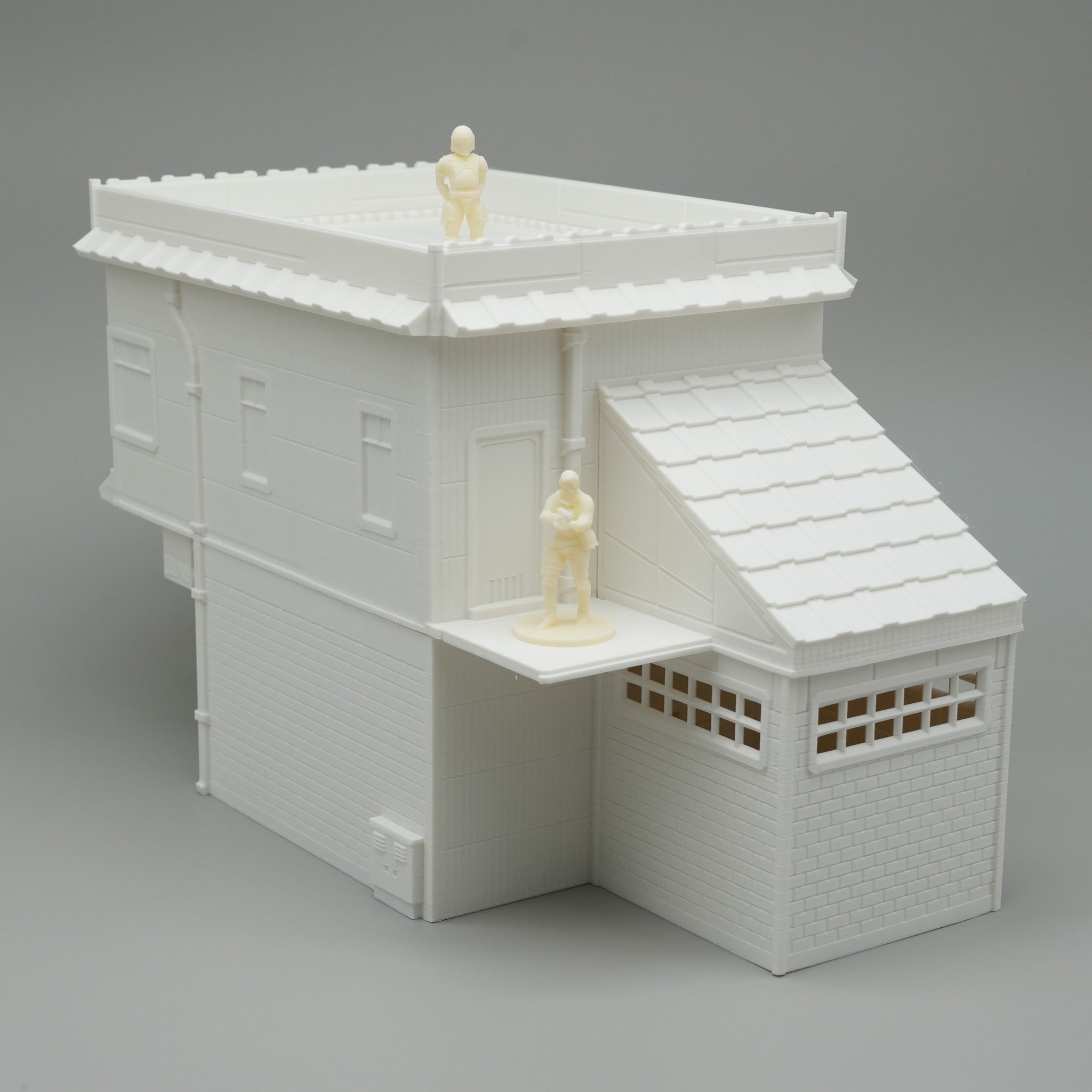 Weißes, modernes Modellhaus mit Flachdach und überdachtem Eingangsbereich, zwei Miniaturfiguren drauf.