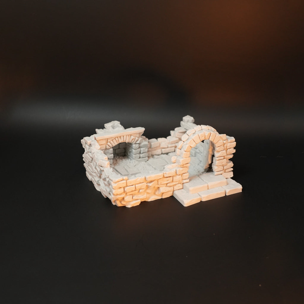 Zerfallenes Torhaus aus grauen und beigen Steinen mit Rundbögen und kleinem Plattformeingang.