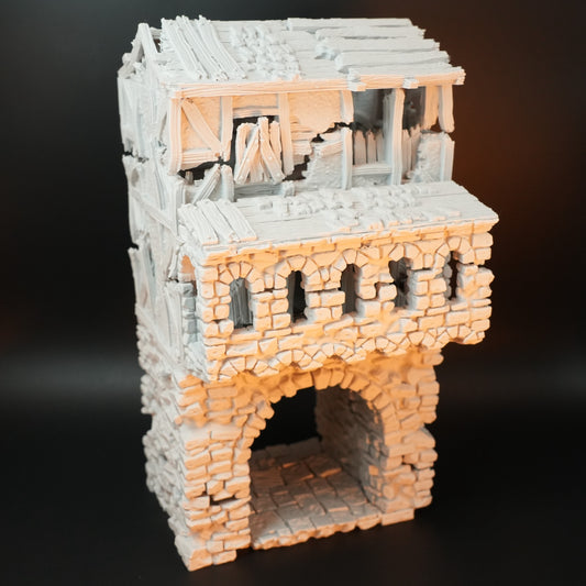 Zweistöckiges zerfallenes Torhaus aus hellgrauem Stein mit offenem Bogen und Holzresten im oberen Bereich.