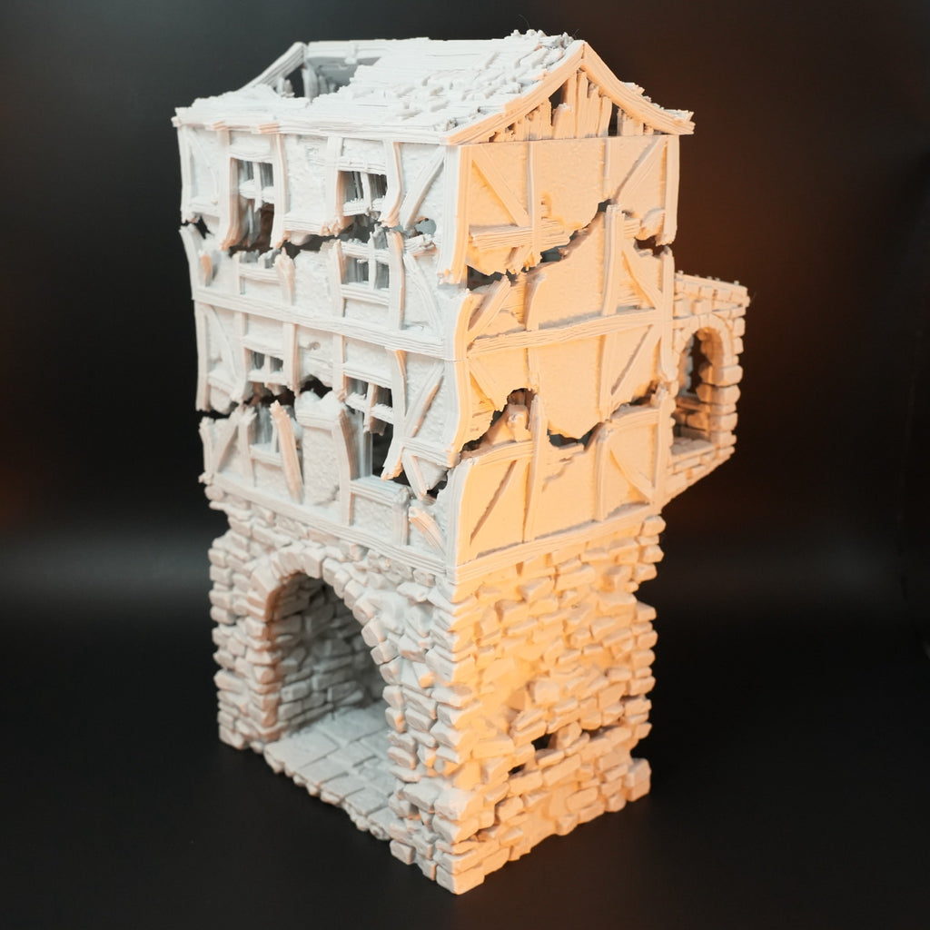 Weißes Modell eines verfallenen Torhauses aus Stein und Fachwerk mit großem Bogen und beschädigten Wänden.