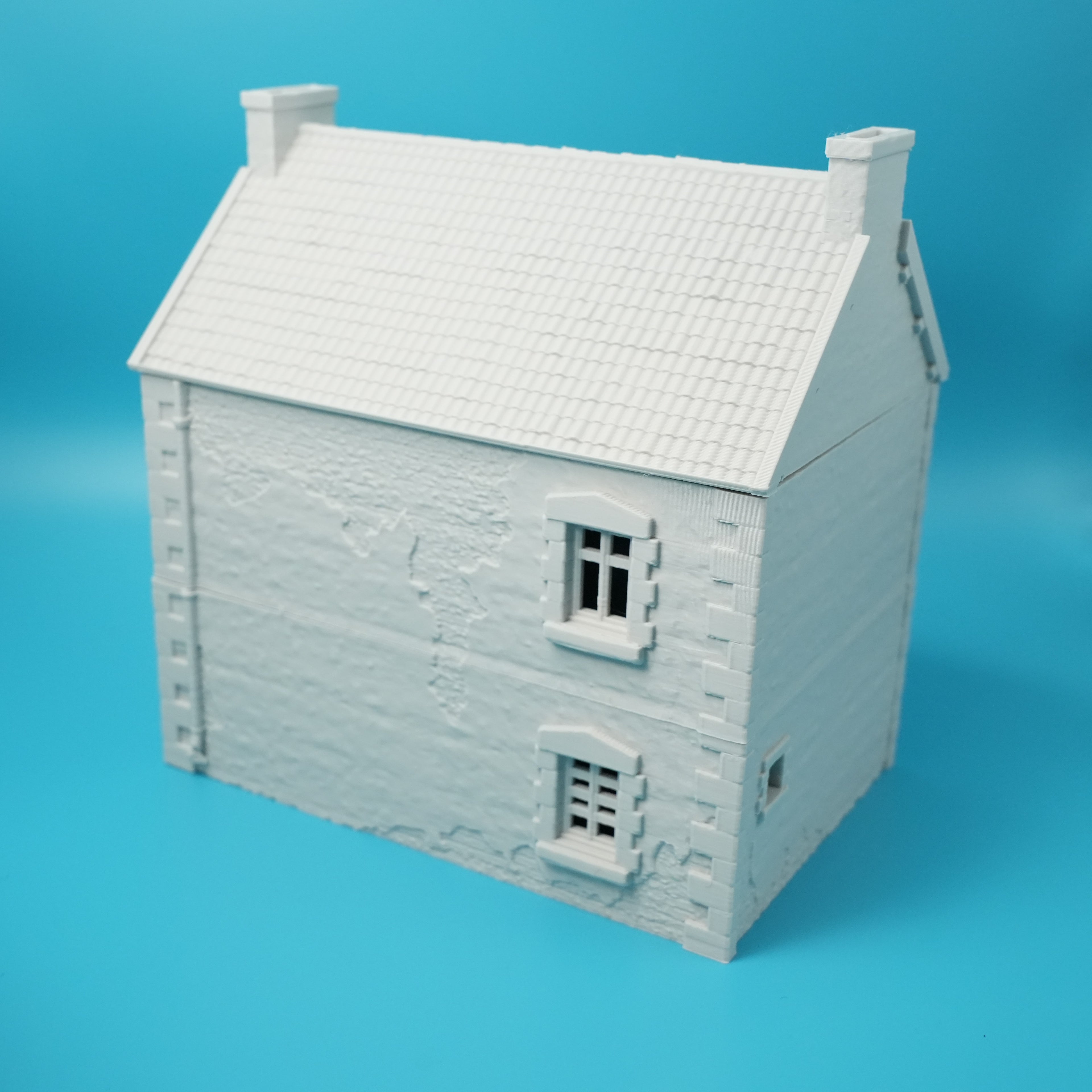 Weißes Modell eines französischen Stadthauses mit Schornsteinen und kleinen Fenstern auf blauem Hintergrund.