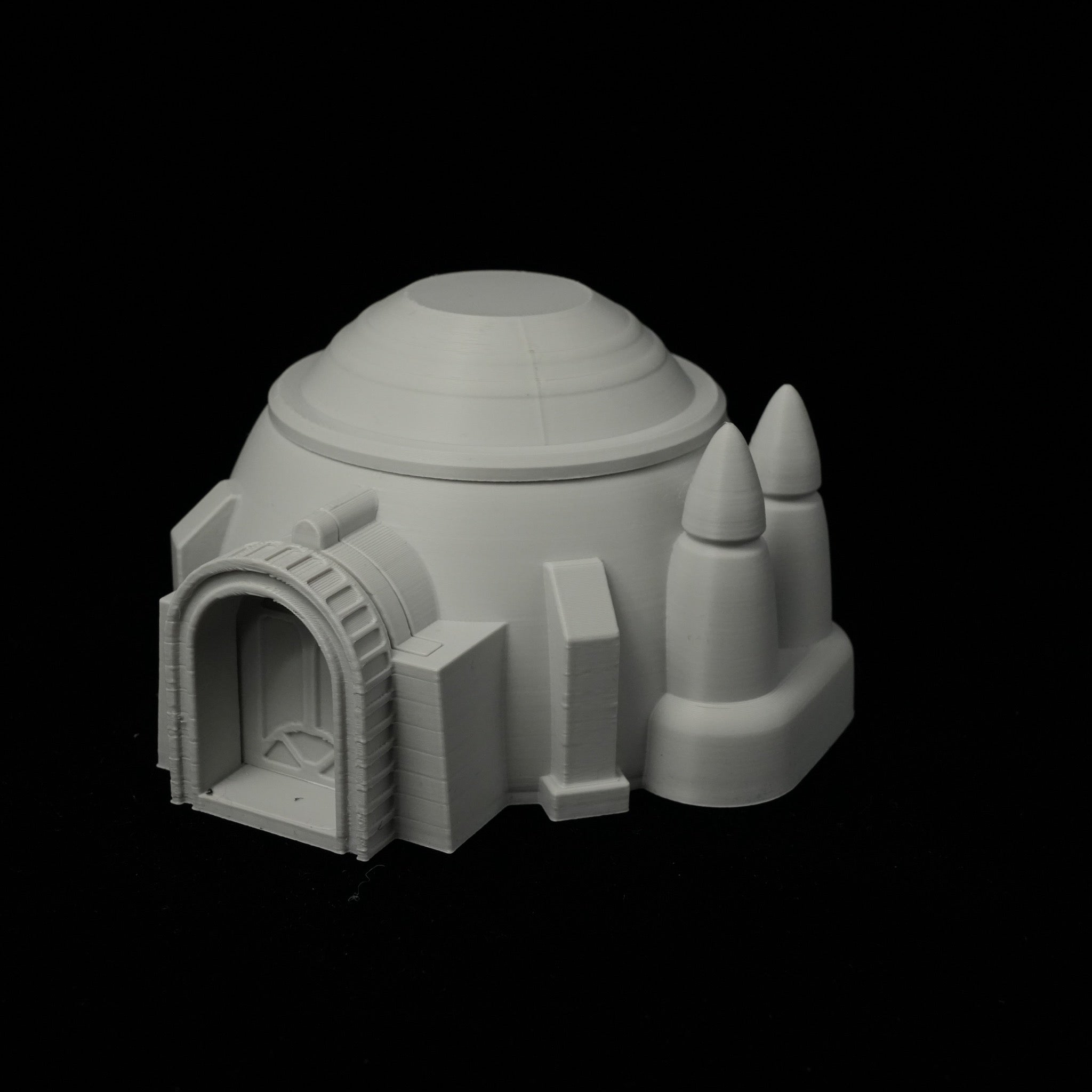 Graues 3D-gedrucktes Wüstenhaus mit rundem Kuppeldach und zwei Turmspitzen auf schwarzem Hintergrund.