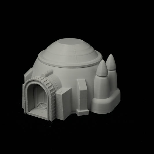 Graues 3D-gedrucktes Wüstenhaus mit rundem Kuppeldach und zwei Turmspitzen auf schwarzem Hintergrund.