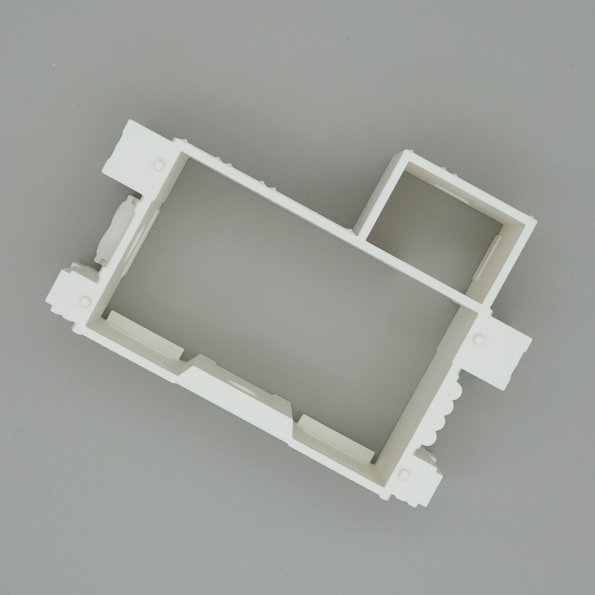 Weißes, rechteckiges Miniatur-Hausmodell mit minimalistischer Raumaufteilung auf grauem Hintergrund.