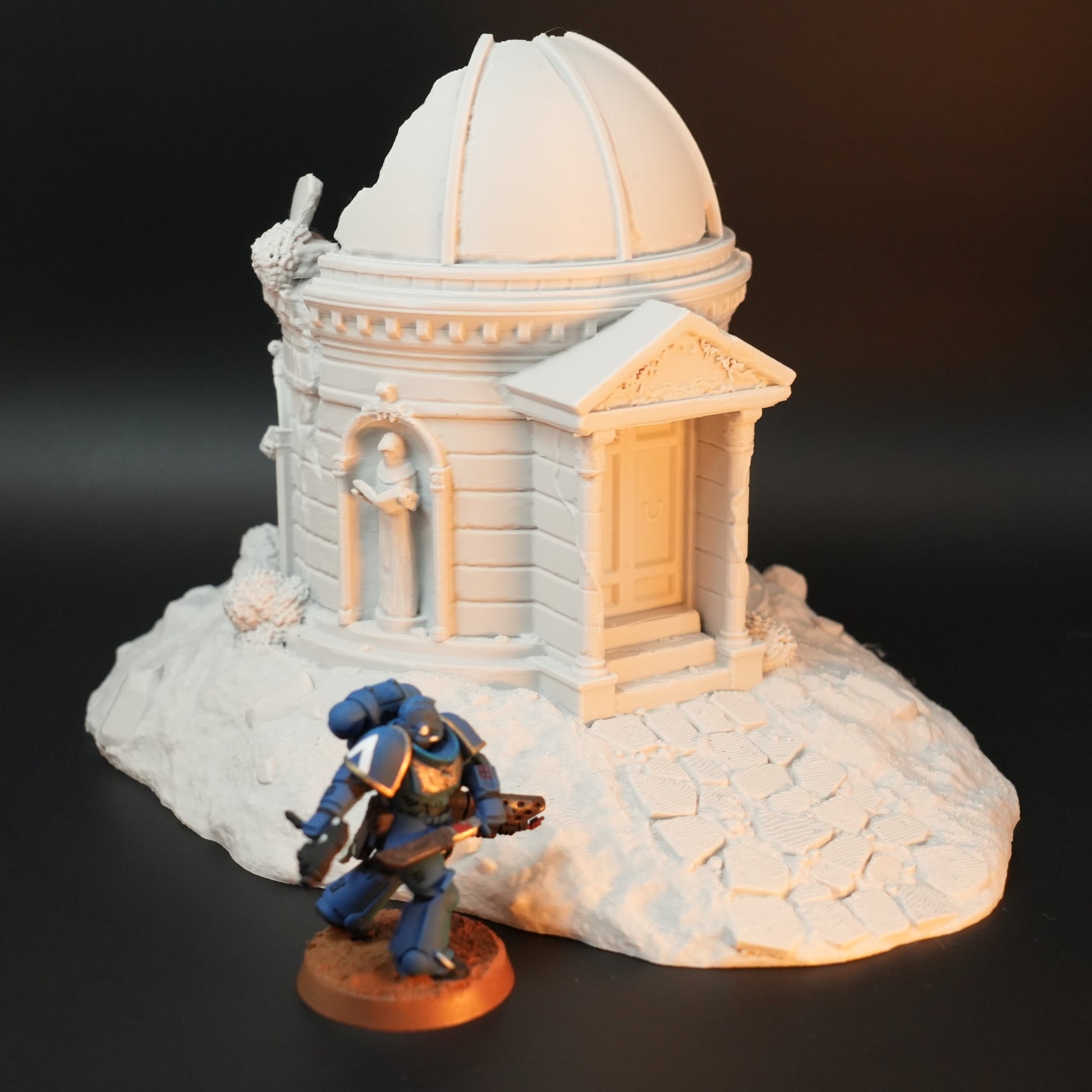 Weißes Mausoleum mit rundem Kuppeldach auf unebener Bodenplatte, mit Miniatur-Figur in blauer Rüstung davor.