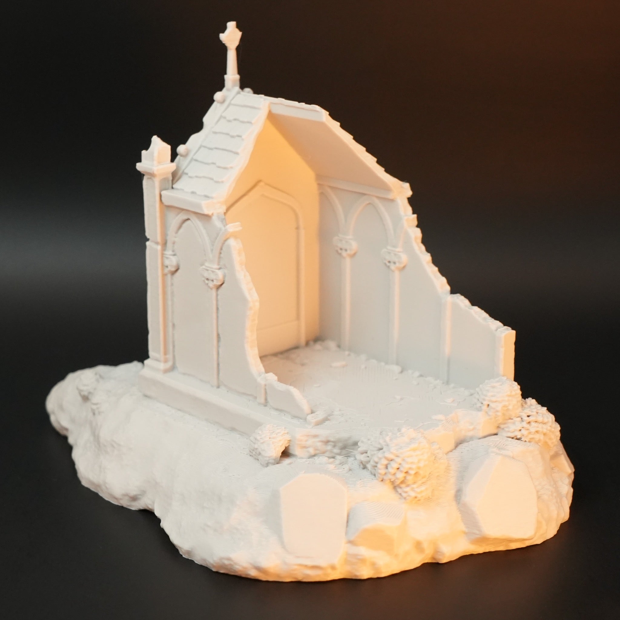 Weißes Modell einer gotischen Gruft mit spitzem Dach, Kreuz auf dem First und steiniger Bodenplatte.