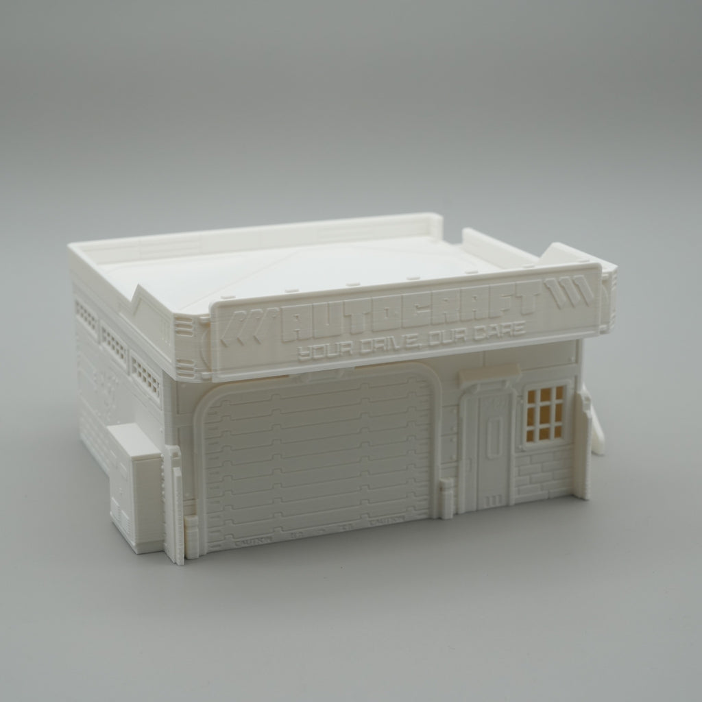 Weißes Modell eines zweistöckigen Werkstattgebäudes mit Rolltor und kleinen Fenstern.