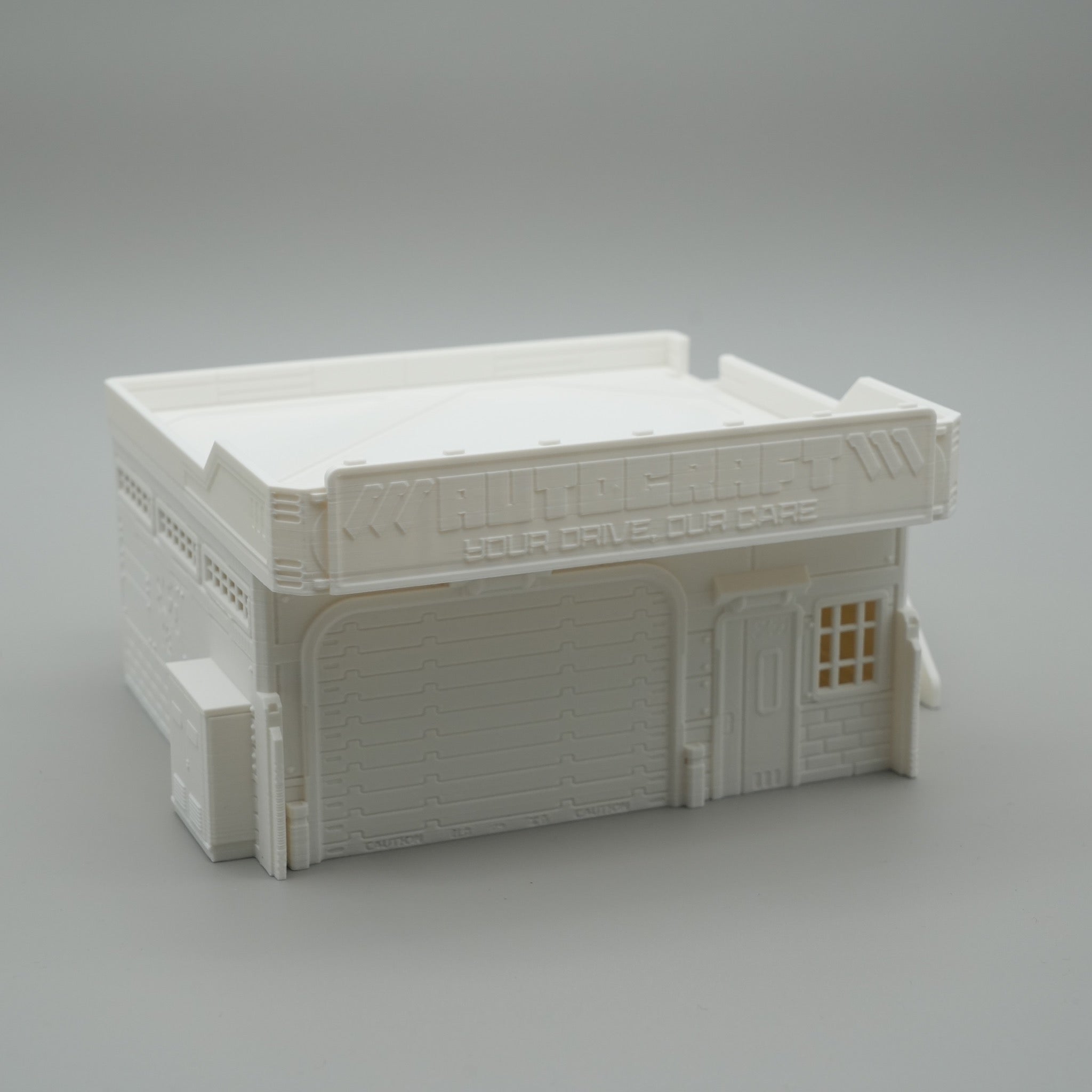 Weißes Modell eines zweistöckigen Werkstattgebäudes mit Rolltor und kleinen Fenstern.