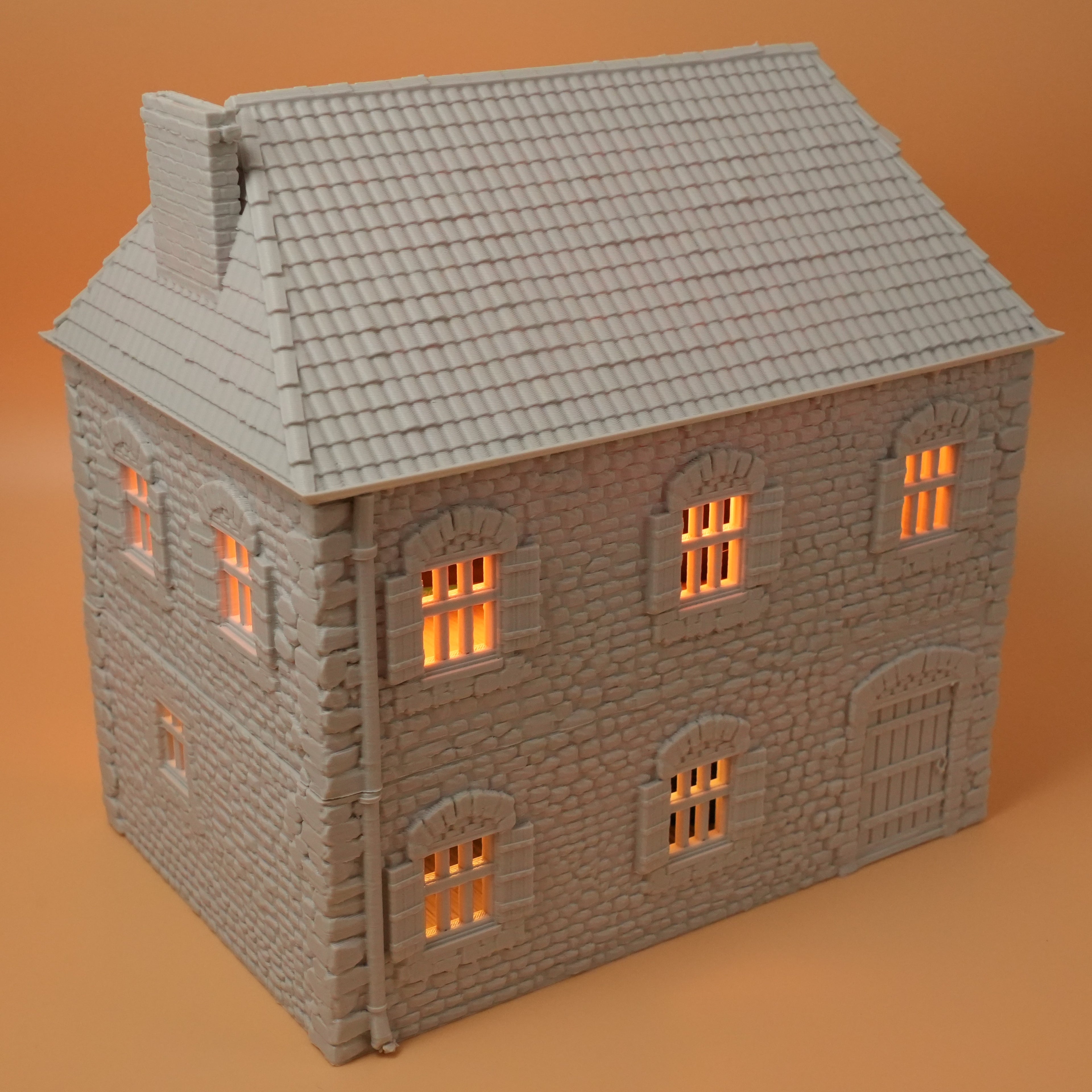 Graues Modell eines französischen Farmhauses aus Stein mit vielen kleinen Fenstern und beleuchtetem Inneren.