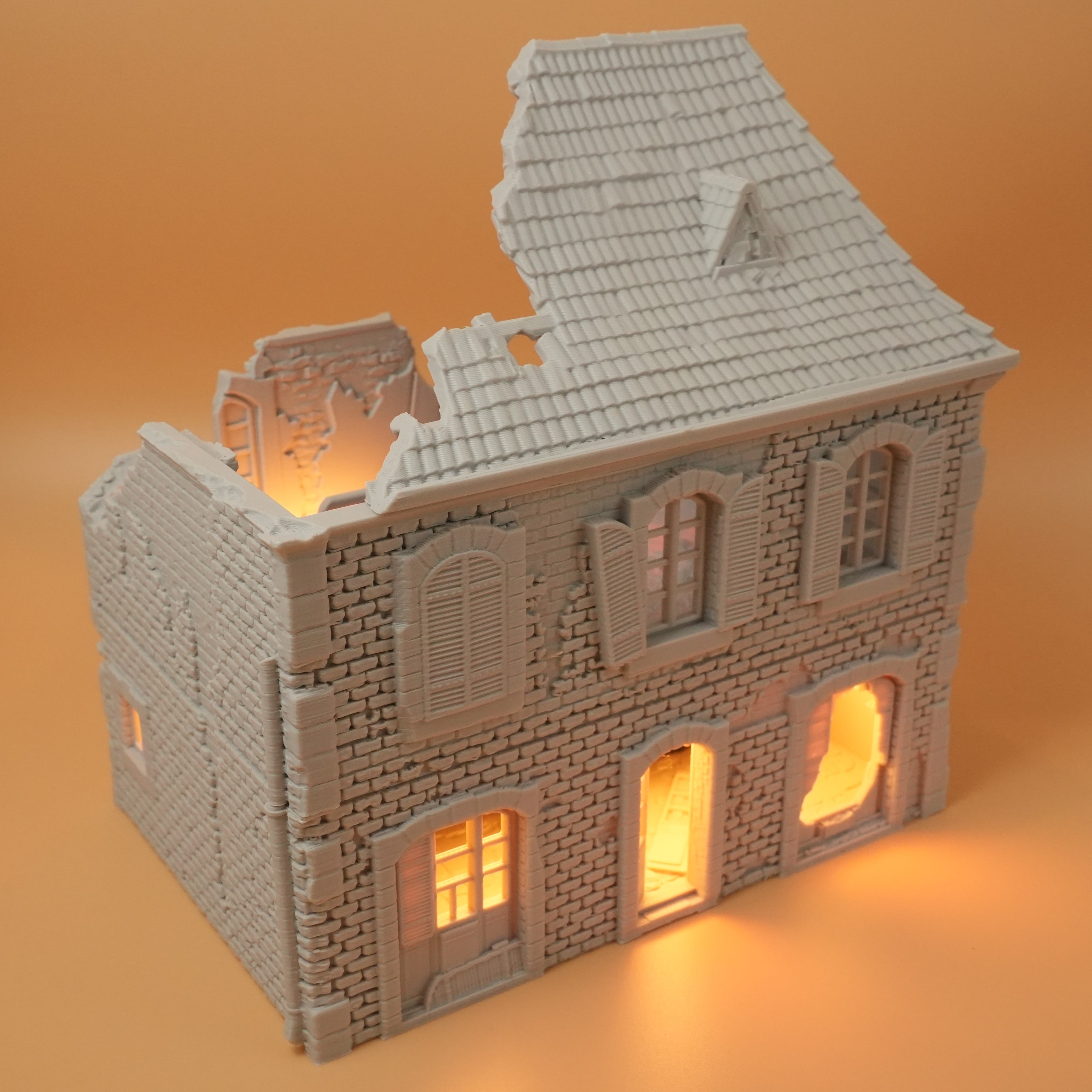 Beige zerfallenes französisches Hausmodell mit zerstörtem Dach und beleuchteten Fenstern.