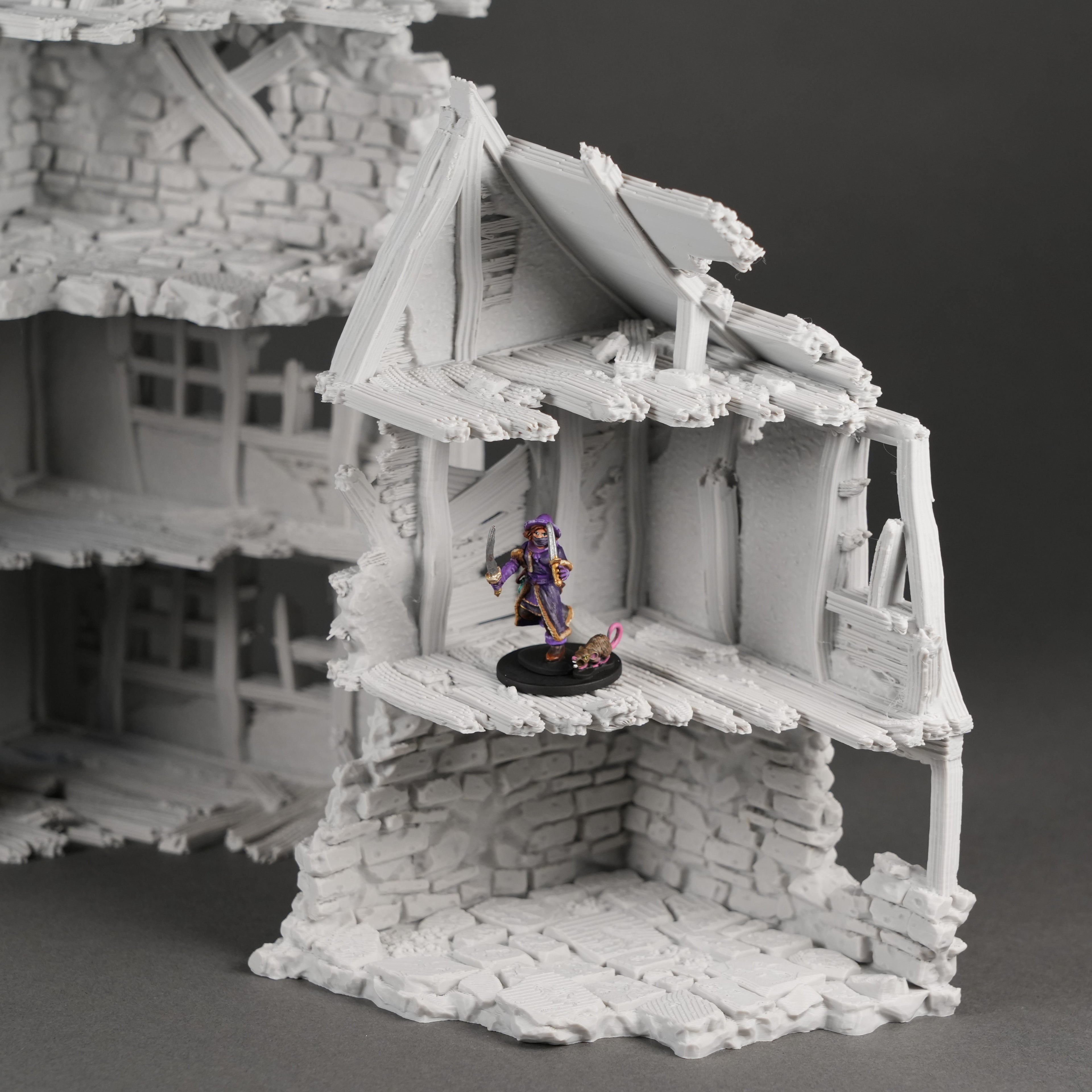 Graue Miniatur Ruine eines zweistöckigen Hauses mit zerstörtem Dach und freiliegenden Balken, 28mm Figur zu Vergleich.