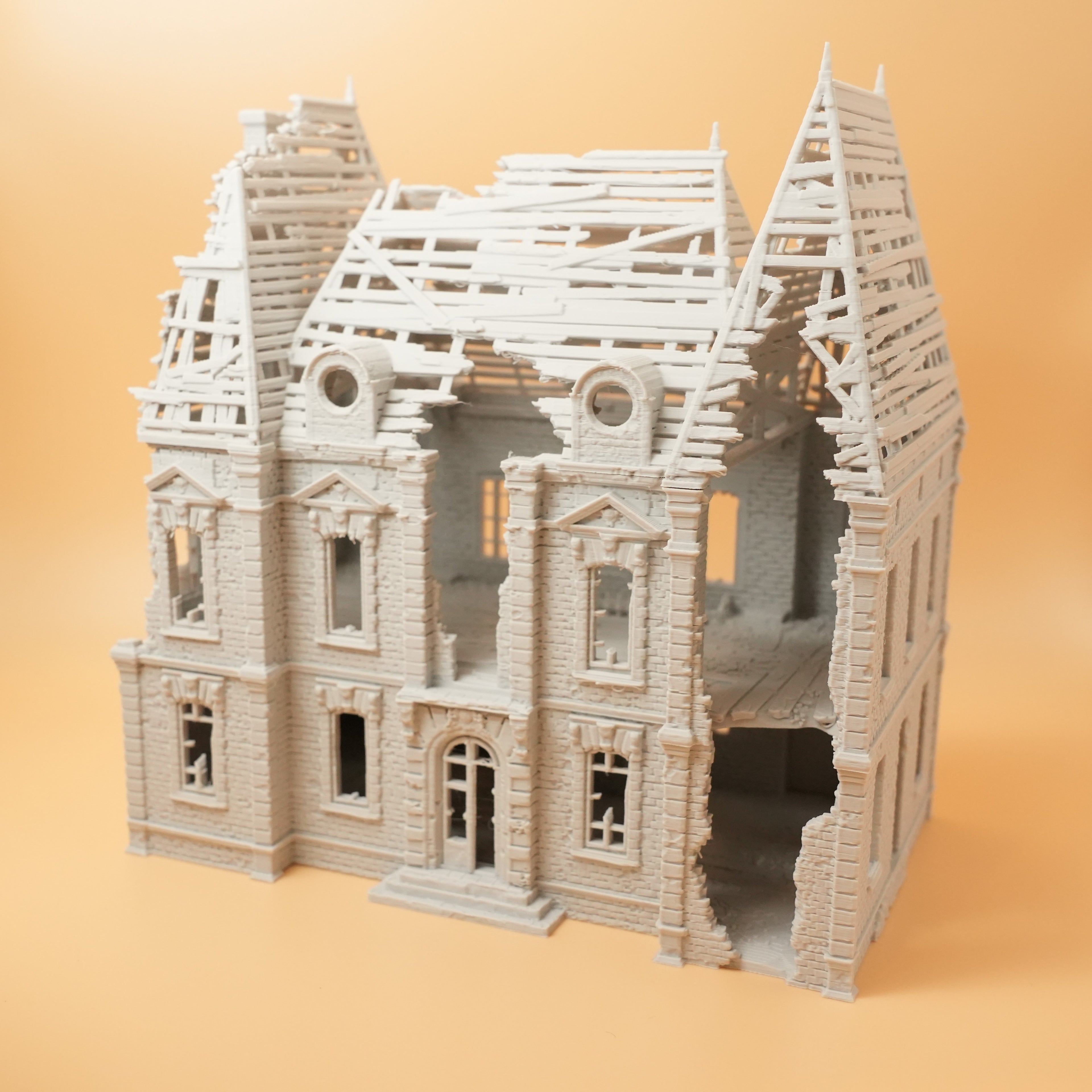 Beige Modell eines zerstörten Herrenhauses mit teilweise eingestürztem Dach und detaillierten Fensterrahmen.