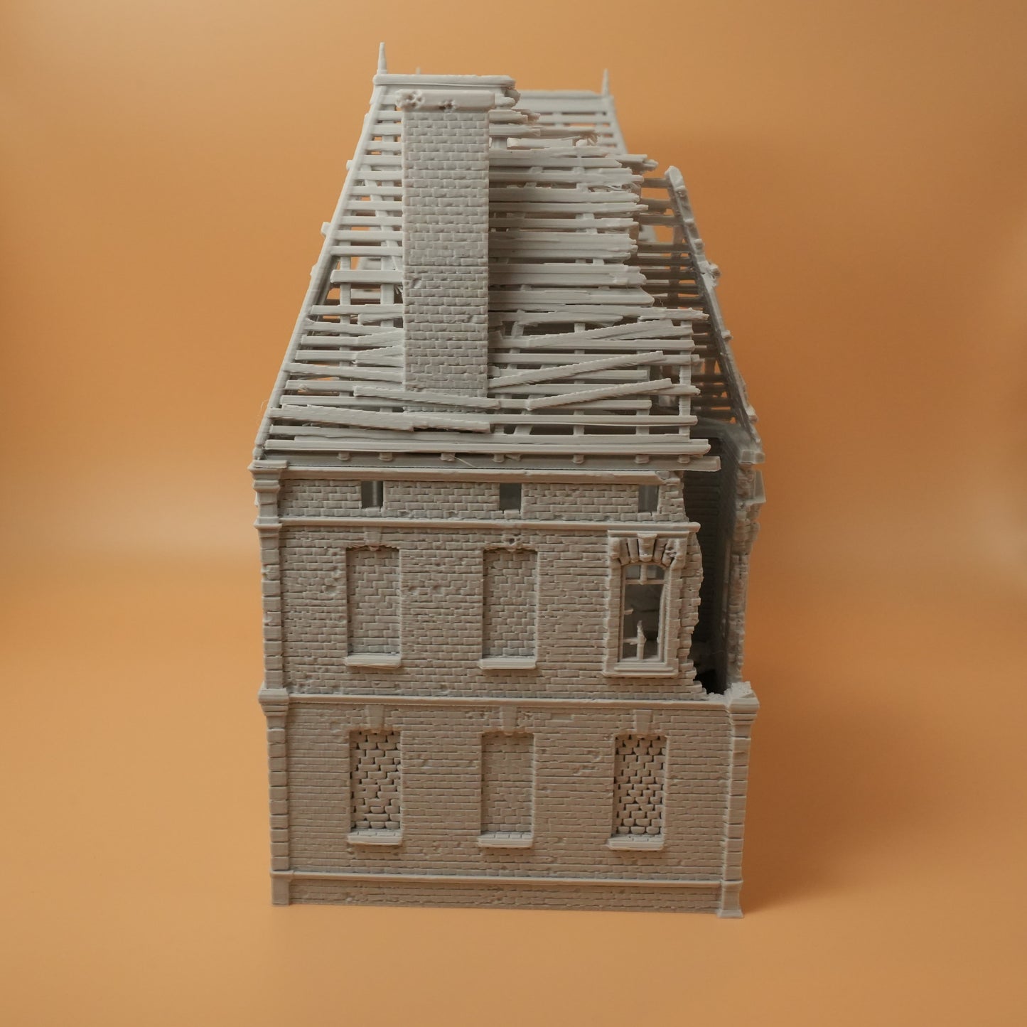 Zweistöckiges Herrenhaus aus grauem Resin mit zerstörtem Dach und beschädigten Fenstern.