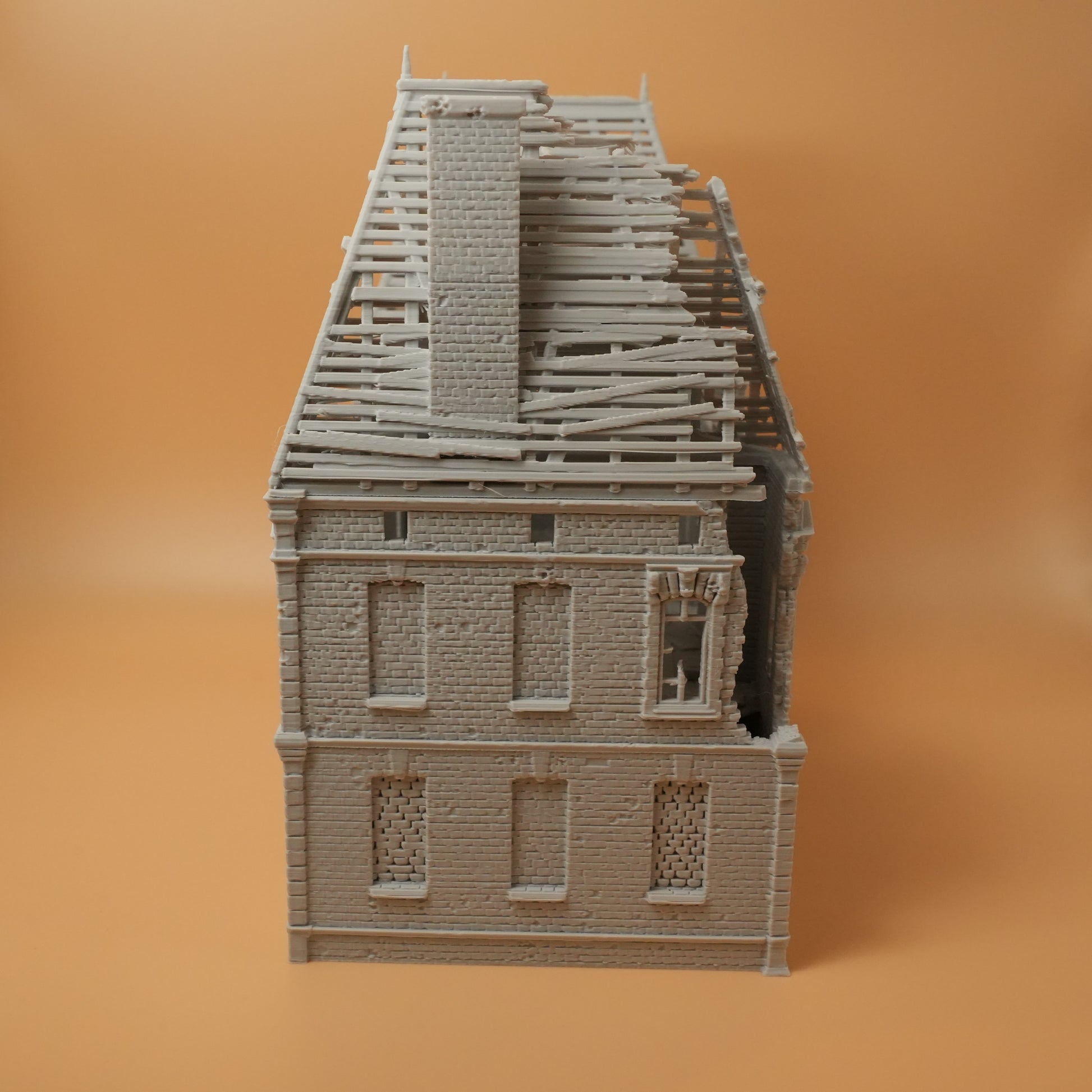 Zweistöckiges Herrenhaus aus grauem Resin mit zerstörtem Dach und beschädigten Fenstern.
