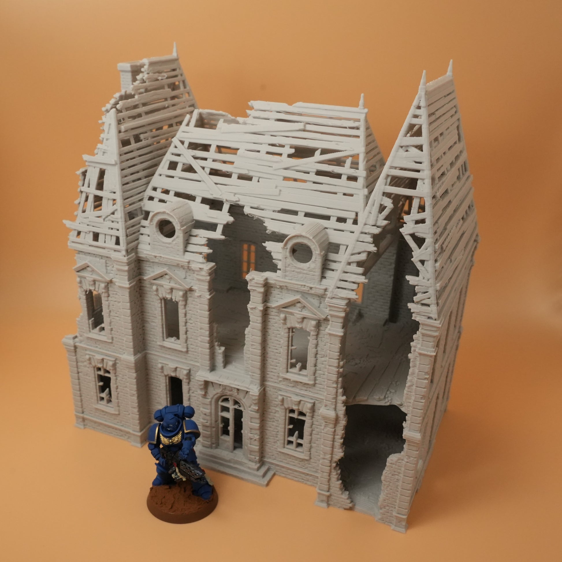 Zerstörtes graues Herrenhaus mit zerbrochenem Dach und fehlenden Wänden, Miniaturfigur davor.