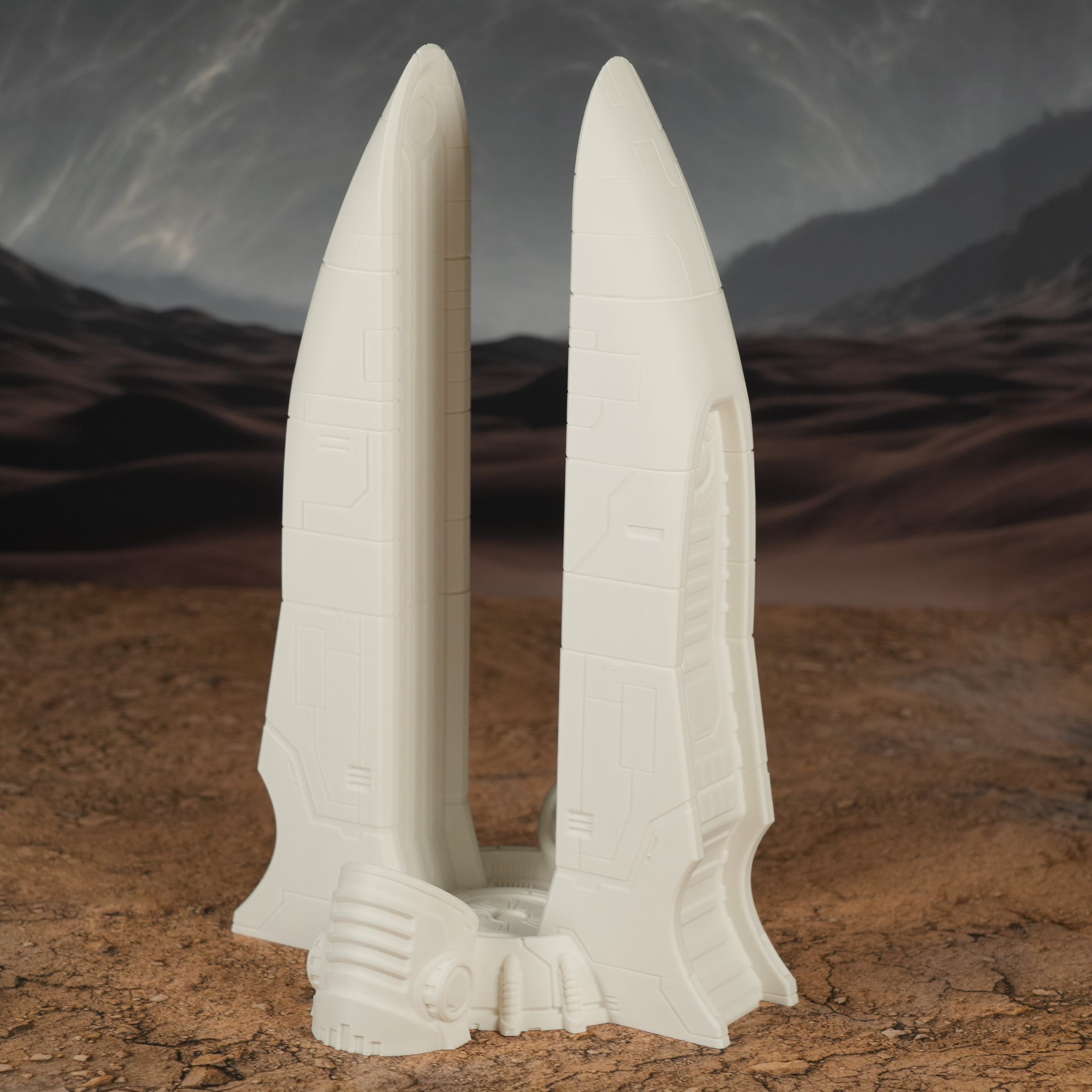 Ockerfarbener, spitzer Turm mit zwei hohen, nebeneinander stehenden Spitzen und Sockel im Wüstenhintergrund.