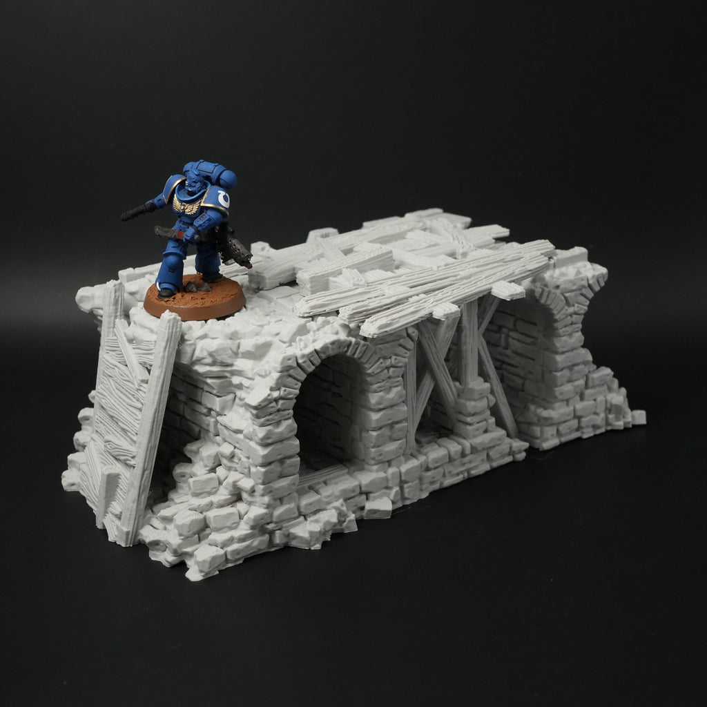 Zerfallene graue Steinbrücke mit zwei Rundbögen und Holzleitern, Miniaturfigur zur Größendarstellung.