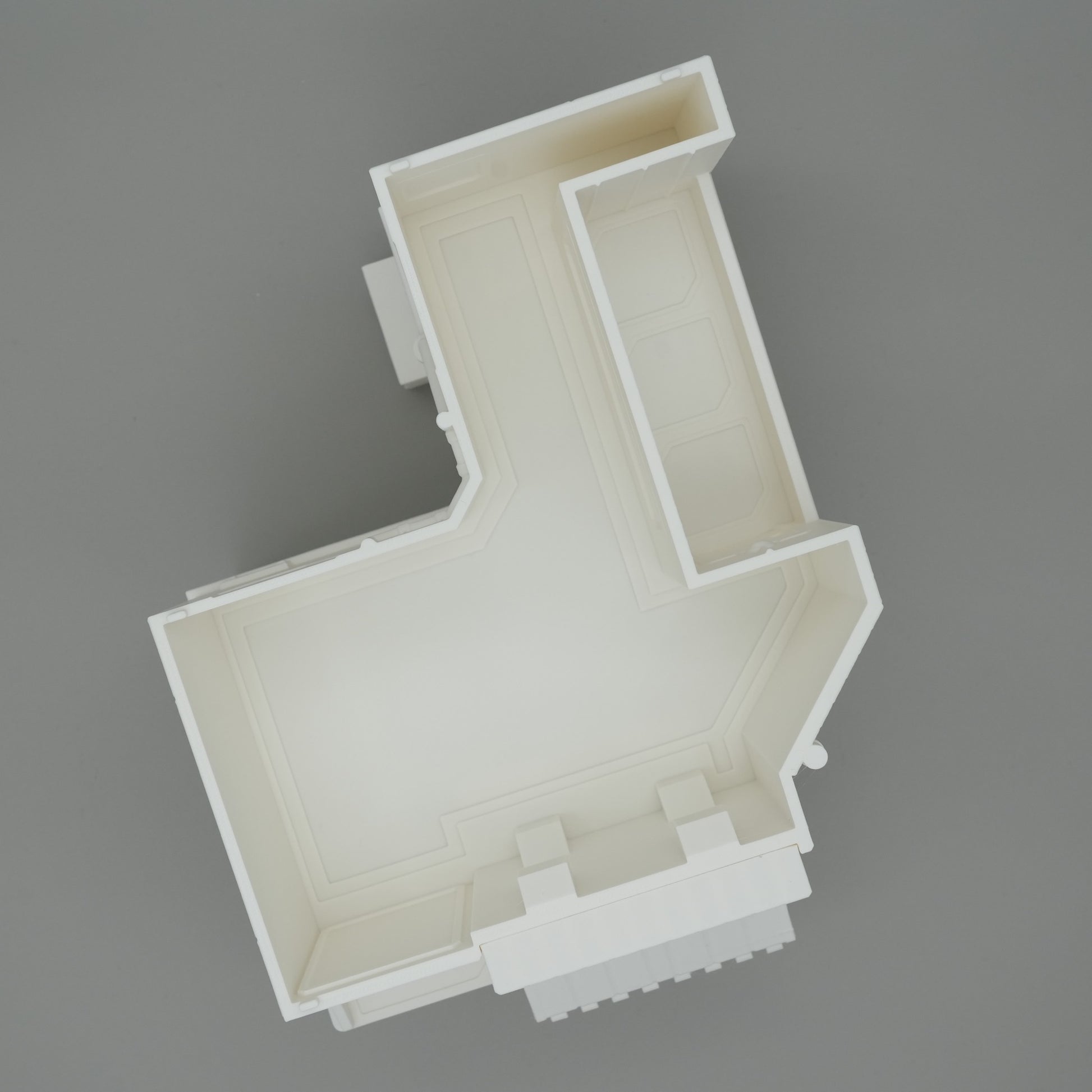 Modell eines weißen Hausgrundrisses mit klaren Wandstrukturen auf grauem Hintergrund.