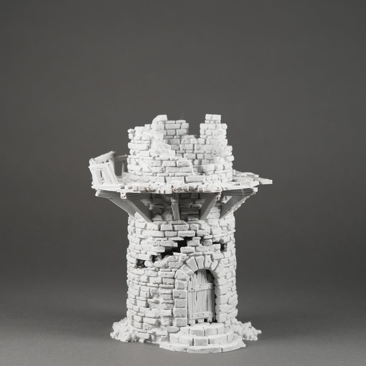 Weißer Miniatur-Turm aus zerfallenen Steinmauern mit rundem Eingang und Kranz am oberen Rand.
