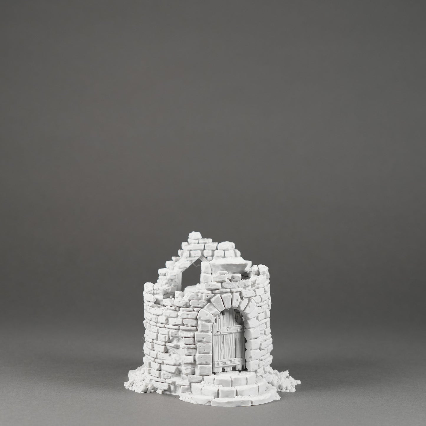 Grau-weißer Modell-Turm mit zerfallener Steinstruktur und Holztür auf rundem Sockel.
