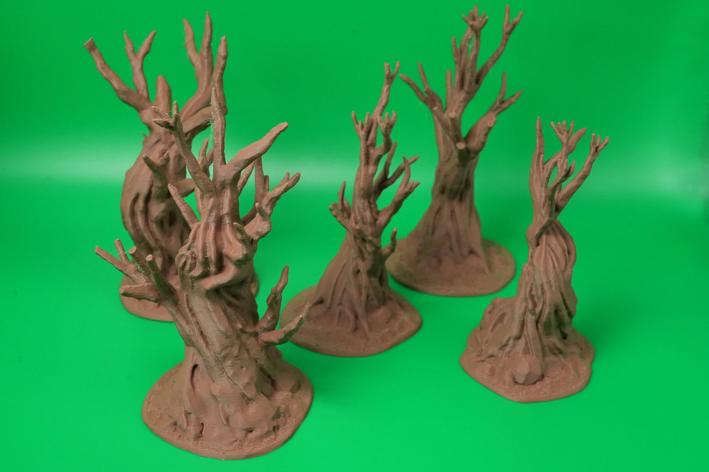 Fünf knorrige Fantasy-Bäume in verschiedenen Größen aus braunem Material vor grünem Hintergrund.