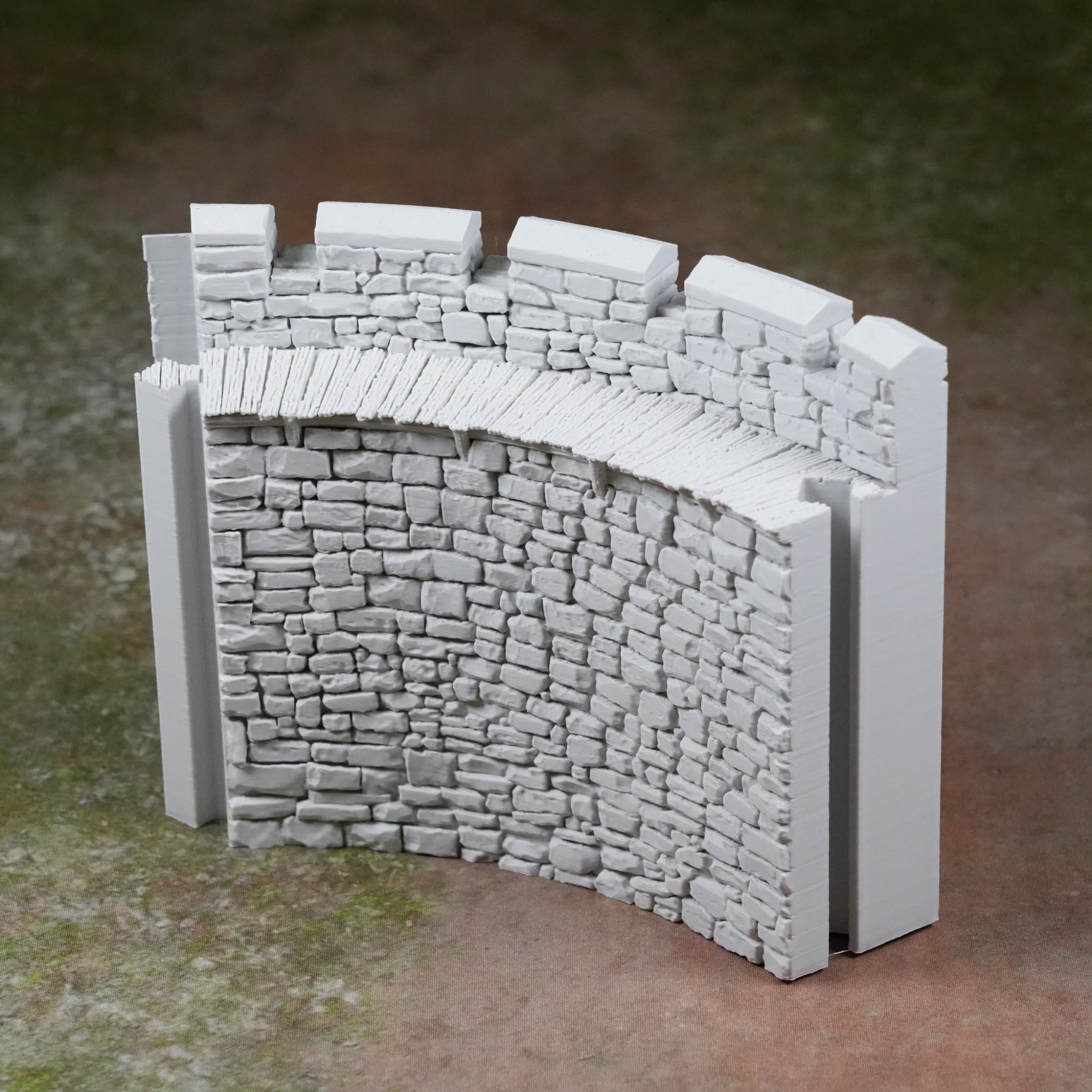 Hellgraue Modell-Burgmauer mit Zinnen und detailreicher Steinstruktur, gebogenes Wandstück.