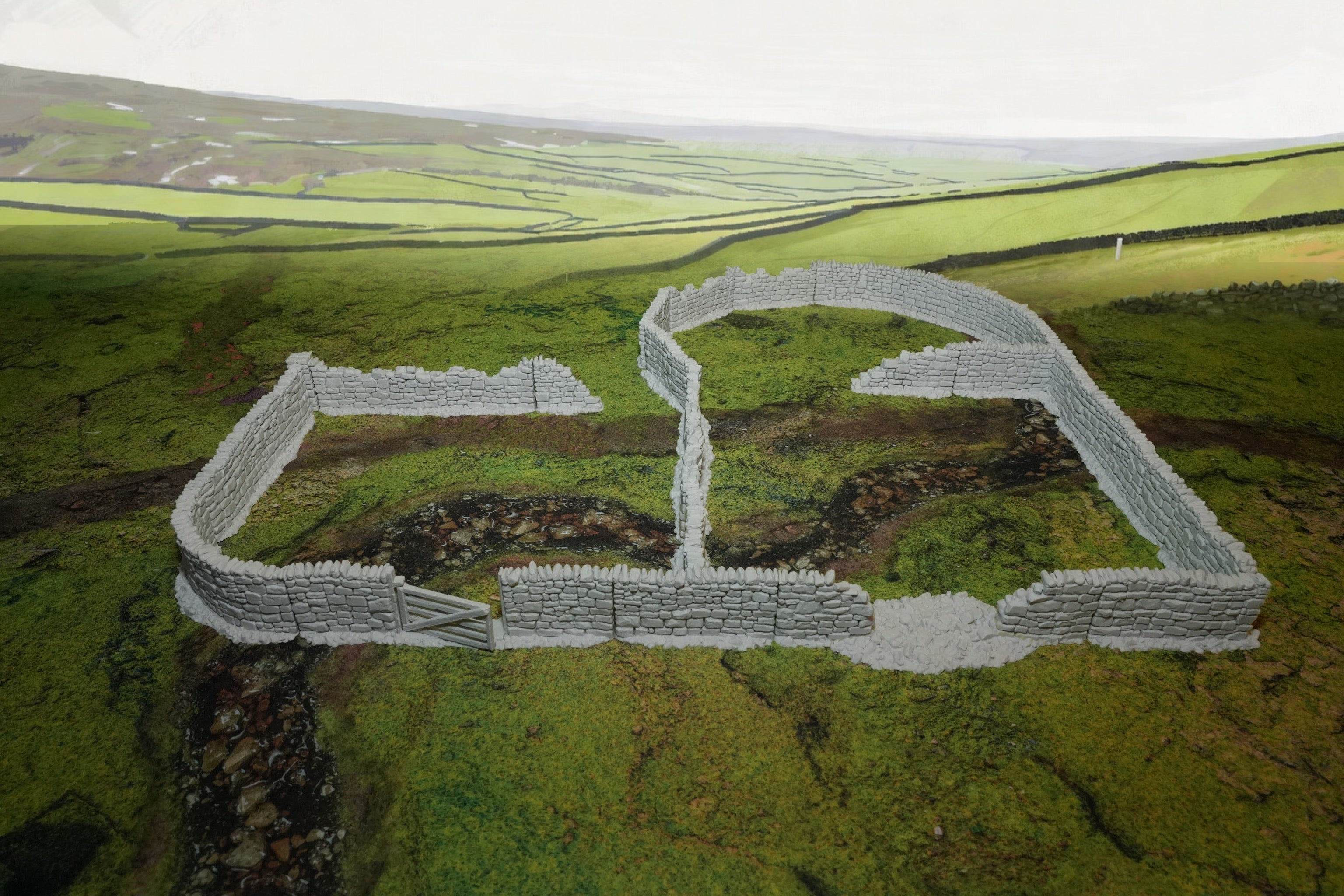 Beige Modell-Steinmauer mit hoher, unregelmäßiger Struktur auf grünem Gelände.