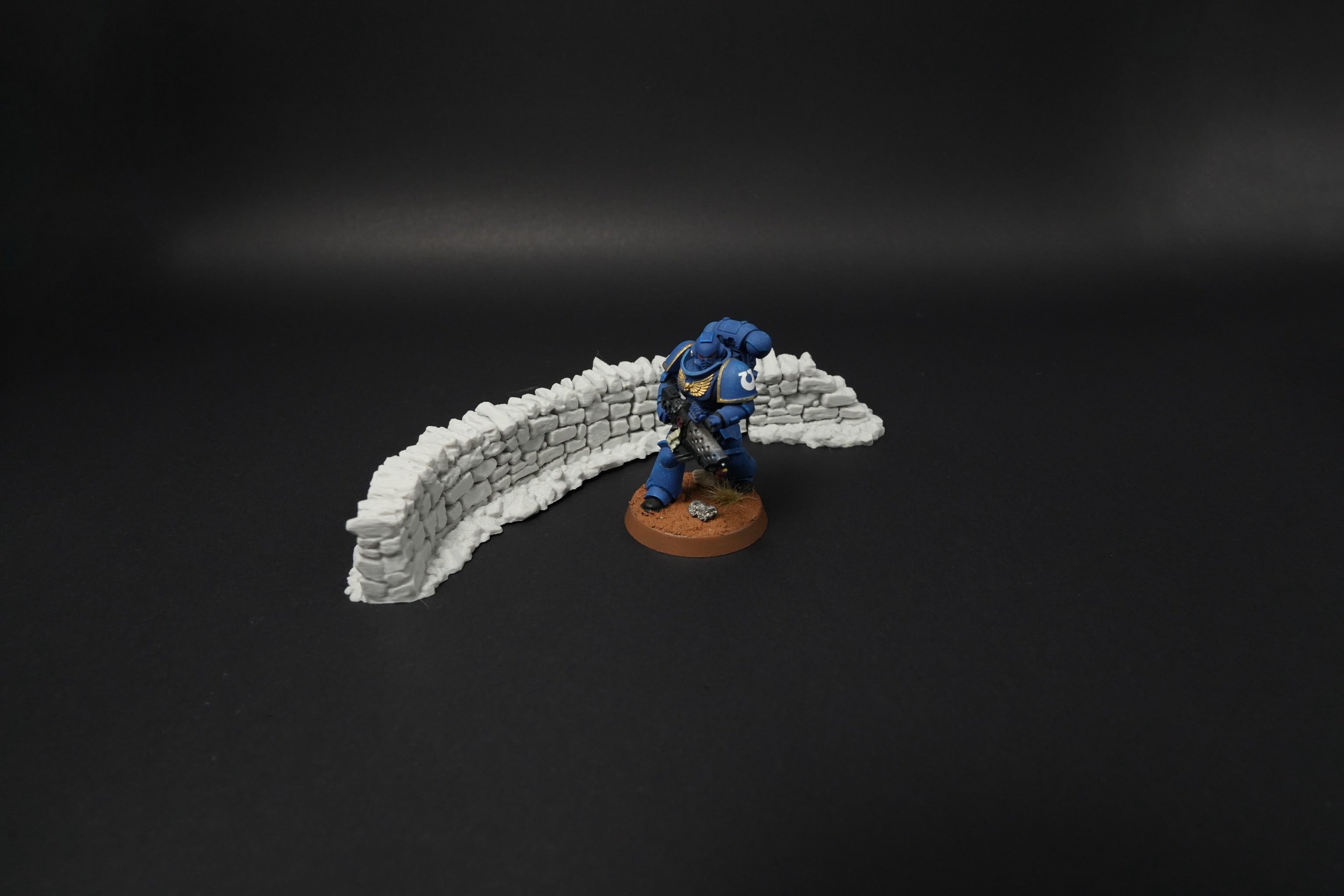 Niedrige weiße Steinmauer in Bogenform mit Miniaturfigur daneben auf schwarzem Hintergrund.